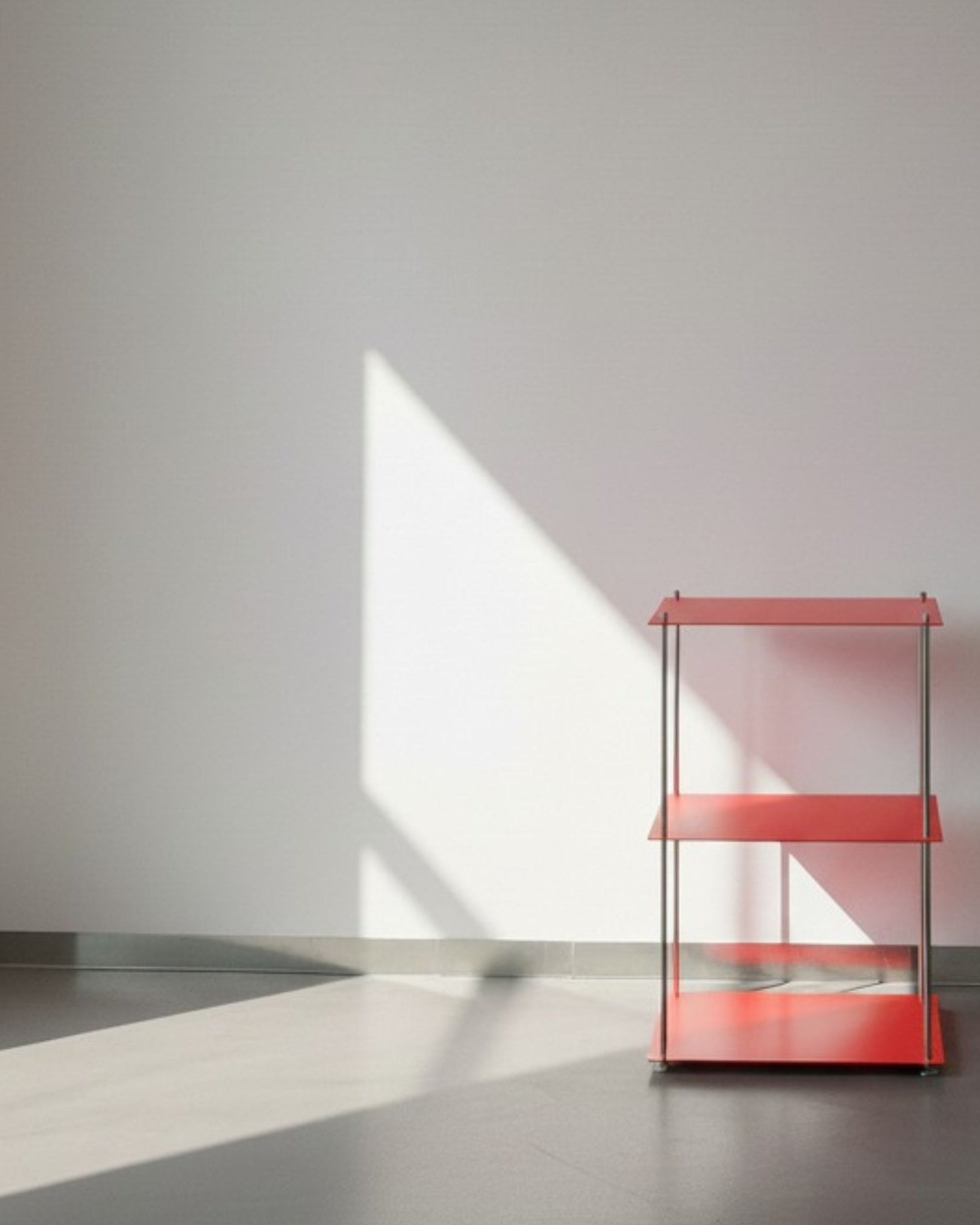 Modulum in leuchtrot mit 3 Fachböden auf grauen Betonboden vor weißer Wand und Lichtspiel