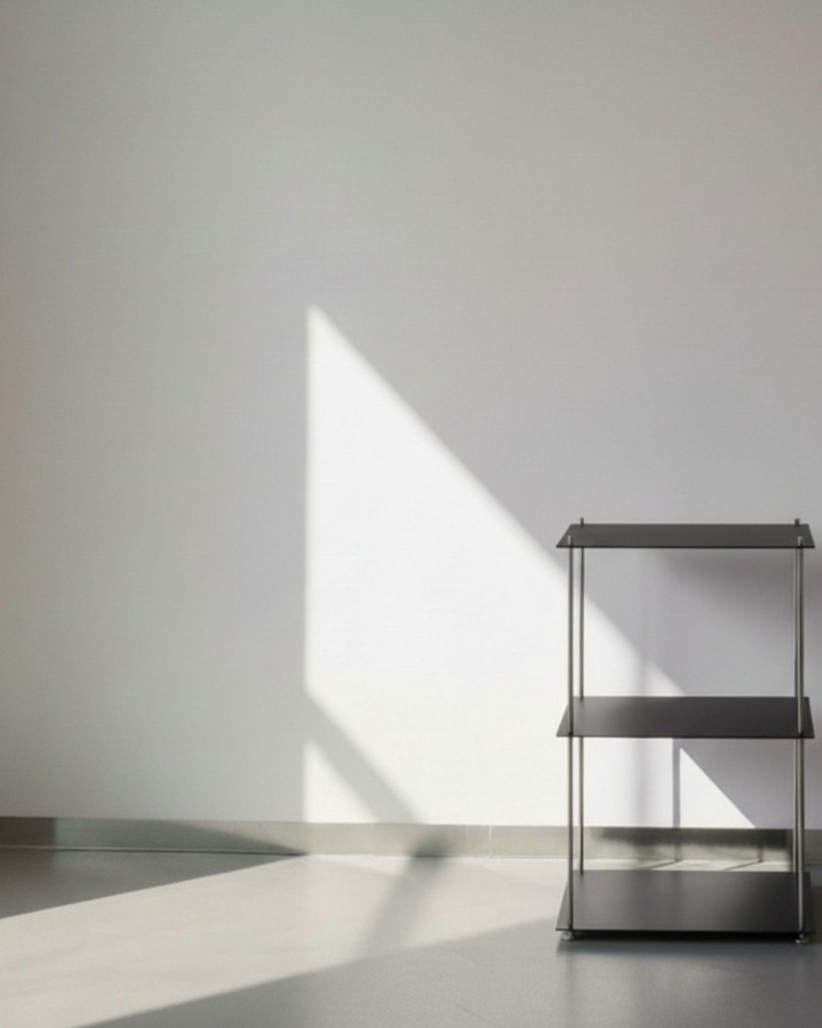 Modulum in schwarz ultramatt mit 3 Fachböden auf grauen Betonboden vor weißer Wand und Lichtspiel