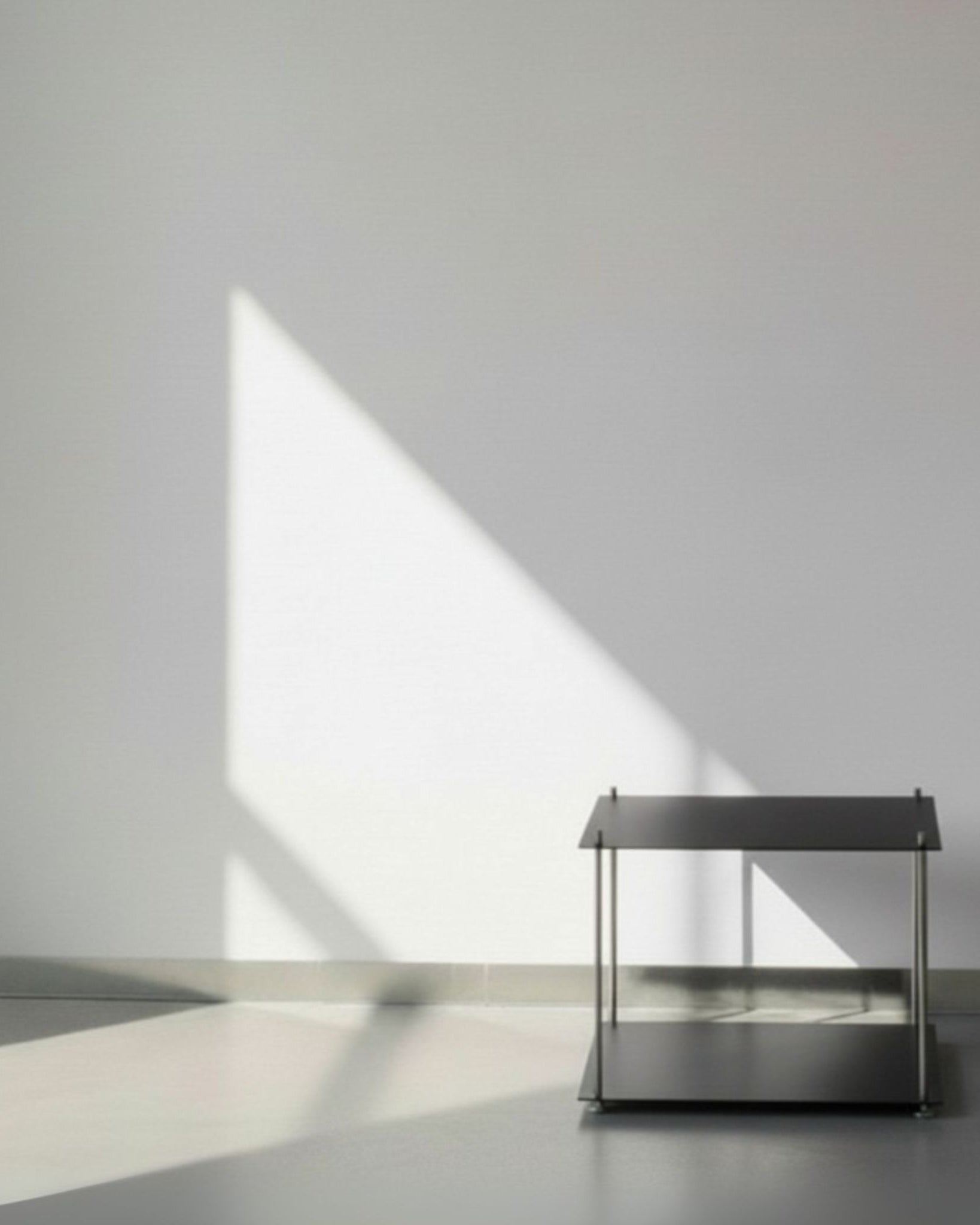 Modulum in schwarz ultramatt mit Basismodul auf grauen Betonboden vor weißer Wand und Lichtspiel