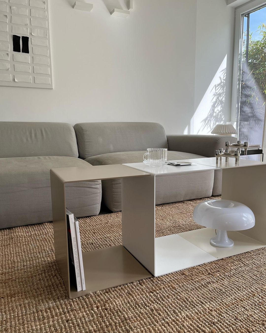 weißer Beistelltisch neben graubiegen Beistelltischals großer Couchtisch, graues Sofa und Rattan-Teppich