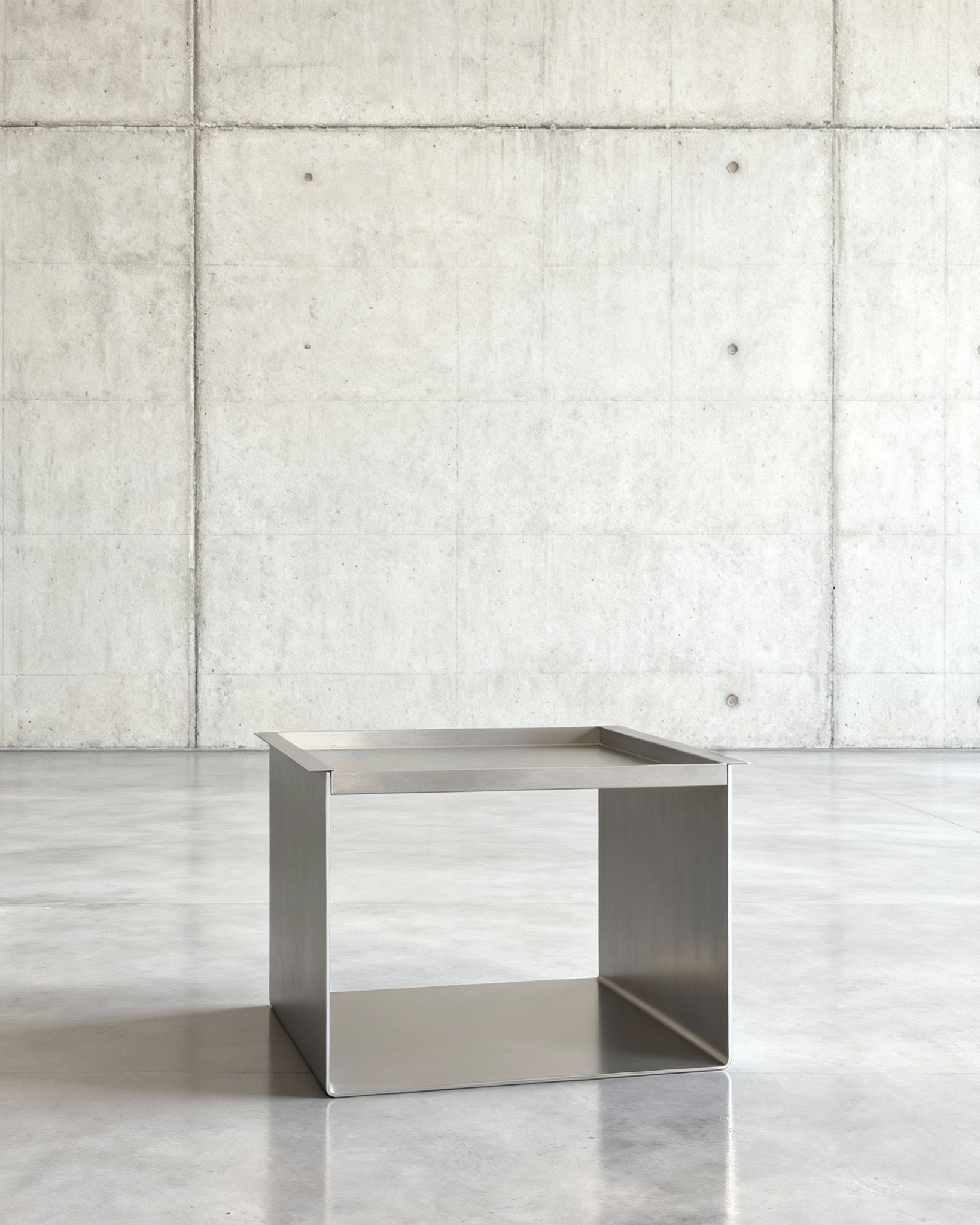 Tray Table Brushed C Beistelltisch in gebürstetem Edelsthahl auf grauen Betonboden vor grauer Betonwand mit Löchern