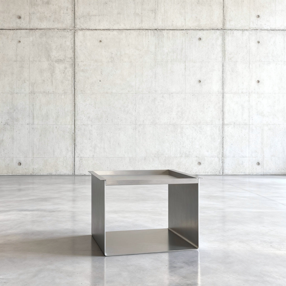 Tray Table Brushed C Beistelltisch in gebürstetem Edelsthahl auf grauen Betonboden vor grauer Betonwand mit Löchern