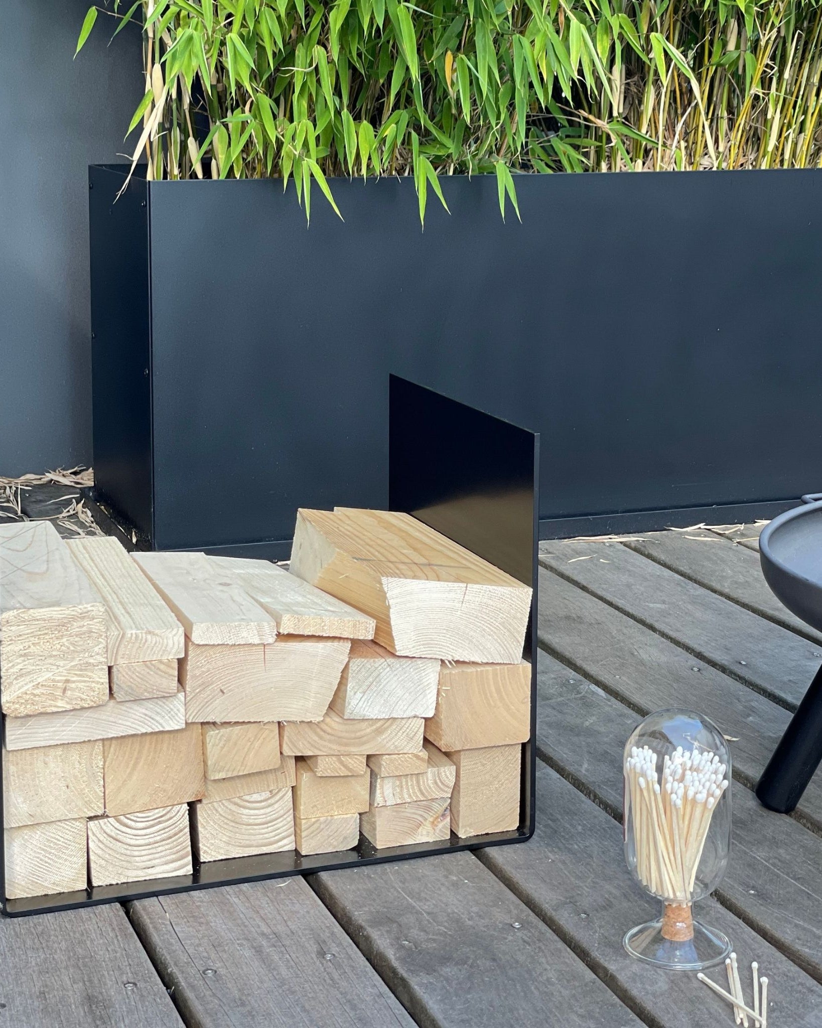 Schwarze Ablage für Feuerholz auf Terrasse neben Feuerschale und Streichhölzern, modernes Outdoor-Design