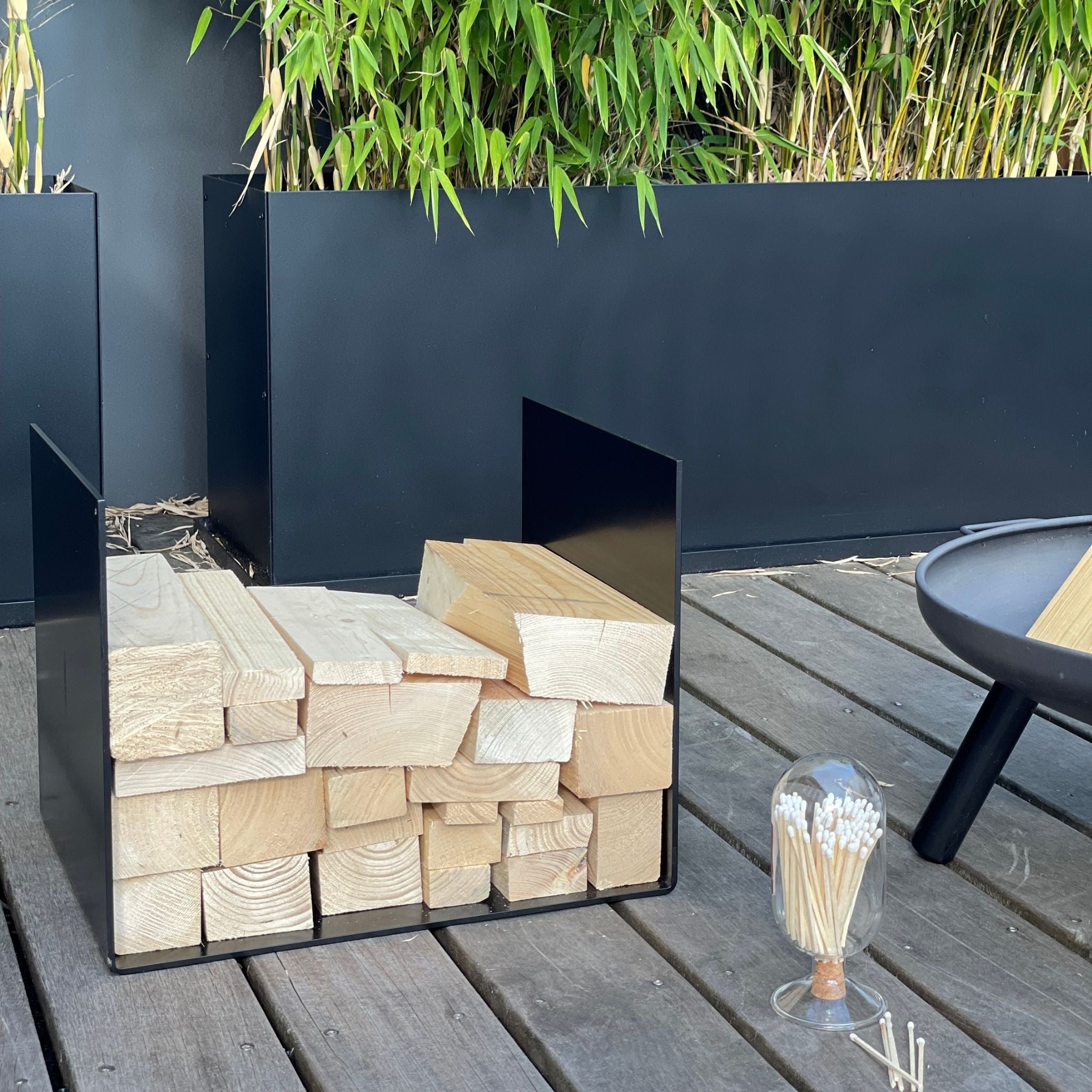 Schwarze Ablage für Feuerholz auf Terrasse neben Feuerschale und Streichhölzern, modernes Outdoor-Design