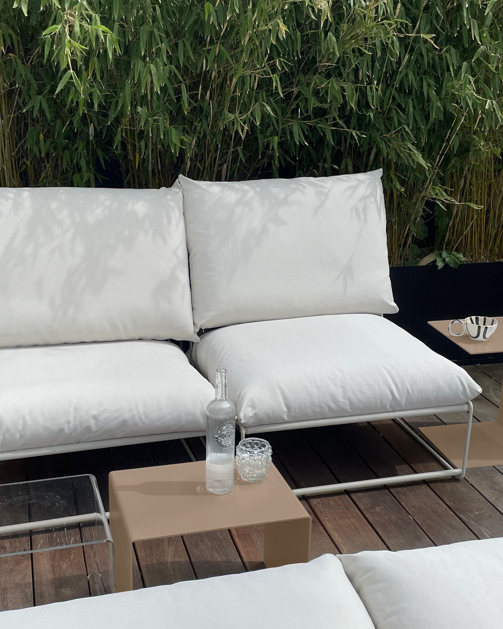 Graubeiger Beistelltisch und Couchtisch neben weißem Outdoor-Loungesofa auf Holzterrasse