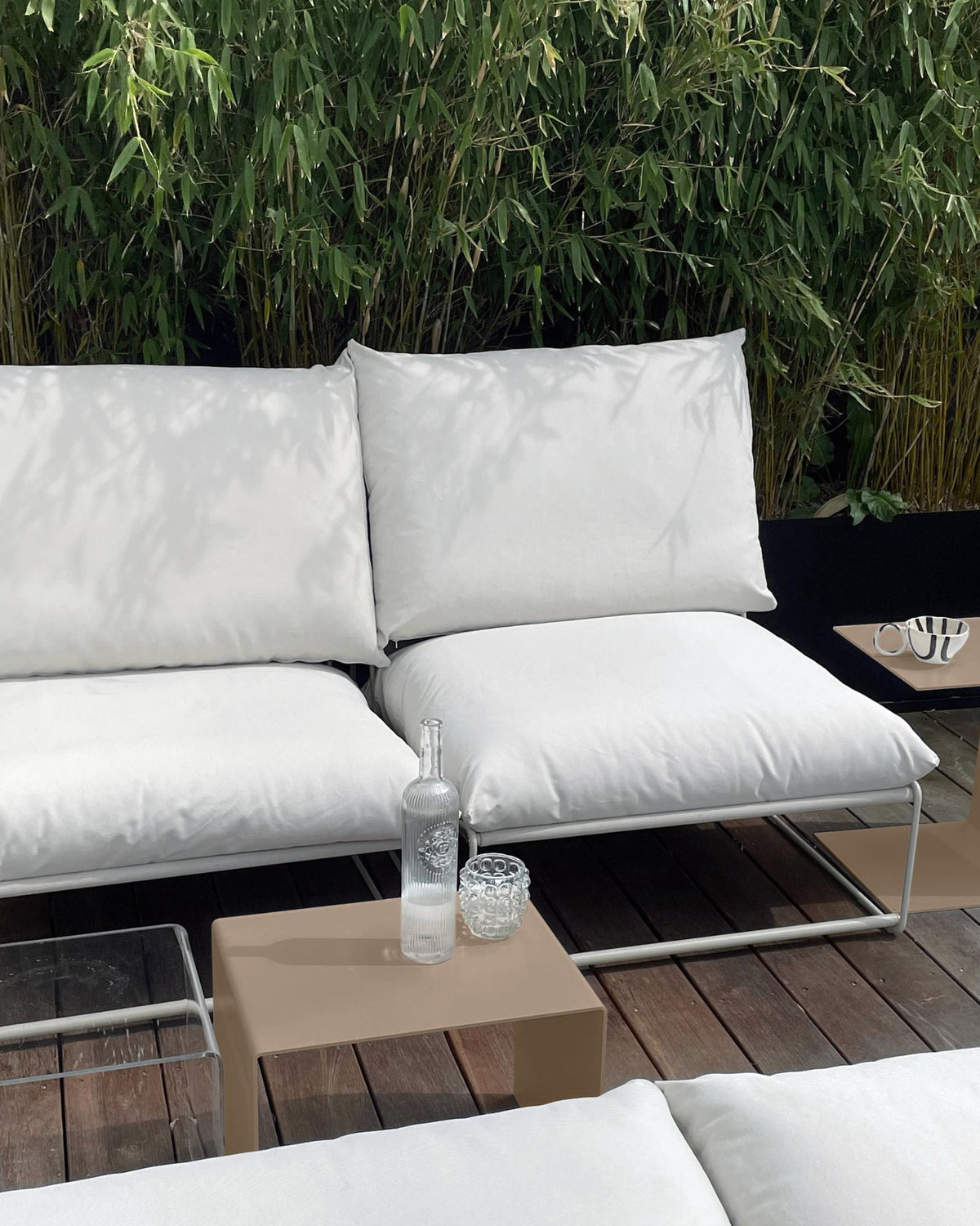 Graubeiger Beistelltisch und Couchtisch neben weißem Outdoor-Loungesofa auf Holzterrasse