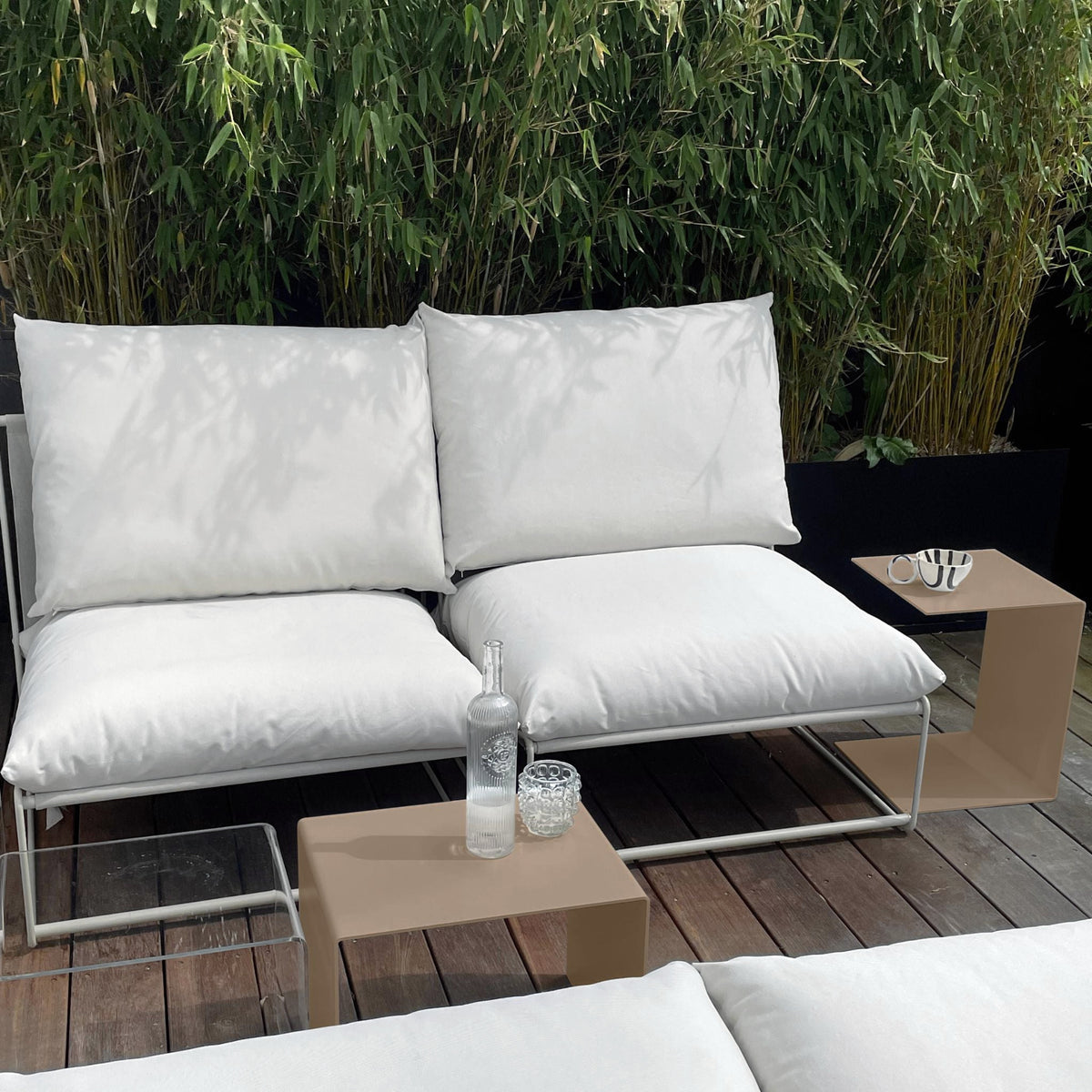 Graubeiger Beistelltisch und Couchtisch neben weißem Outdoor-Loungesofa auf Holzterrasse
