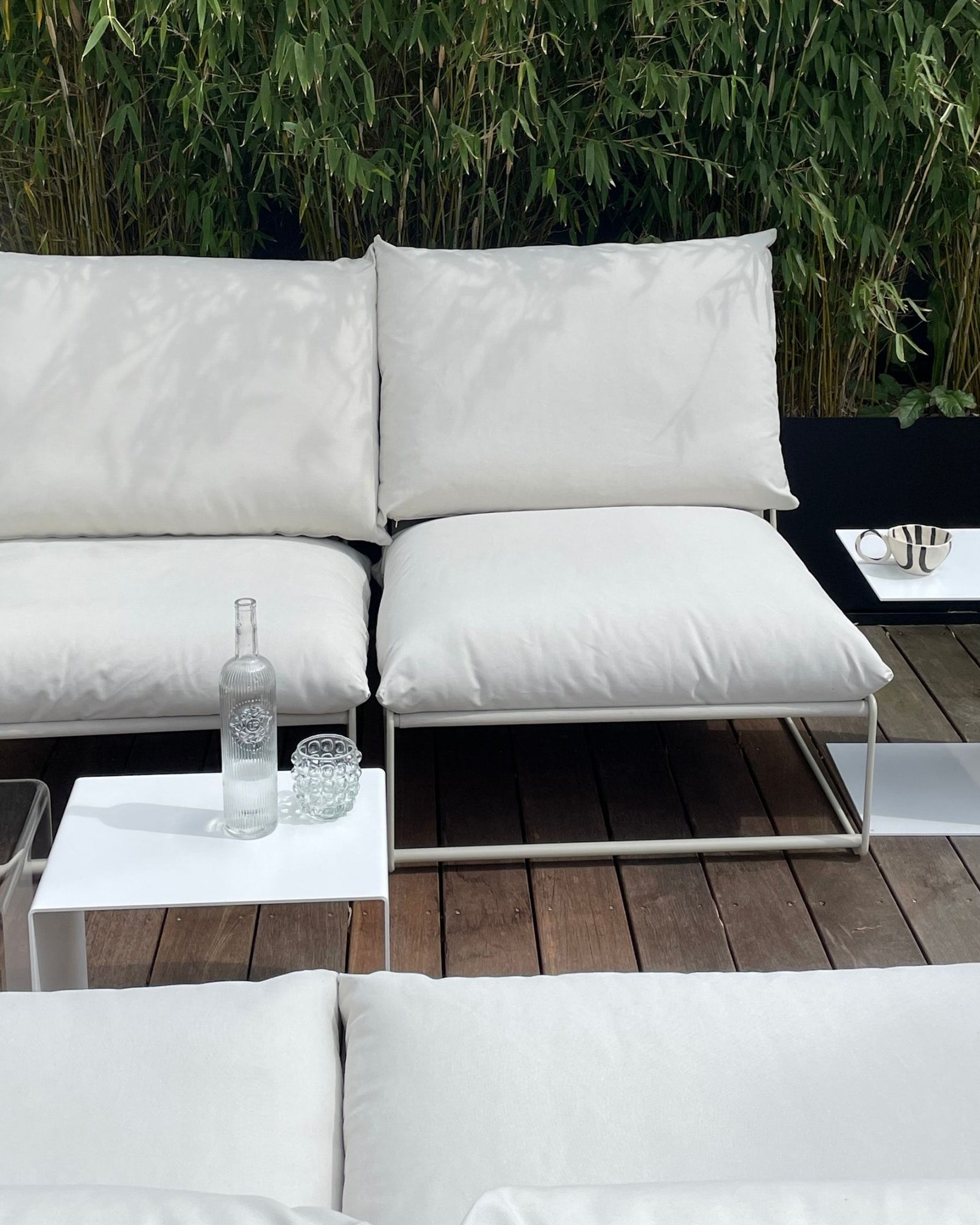 Weiße Beistelltische neben Outdoor-Lounge mit Kissen auf Holzterrasse, modernes Gartenmöbel-Design