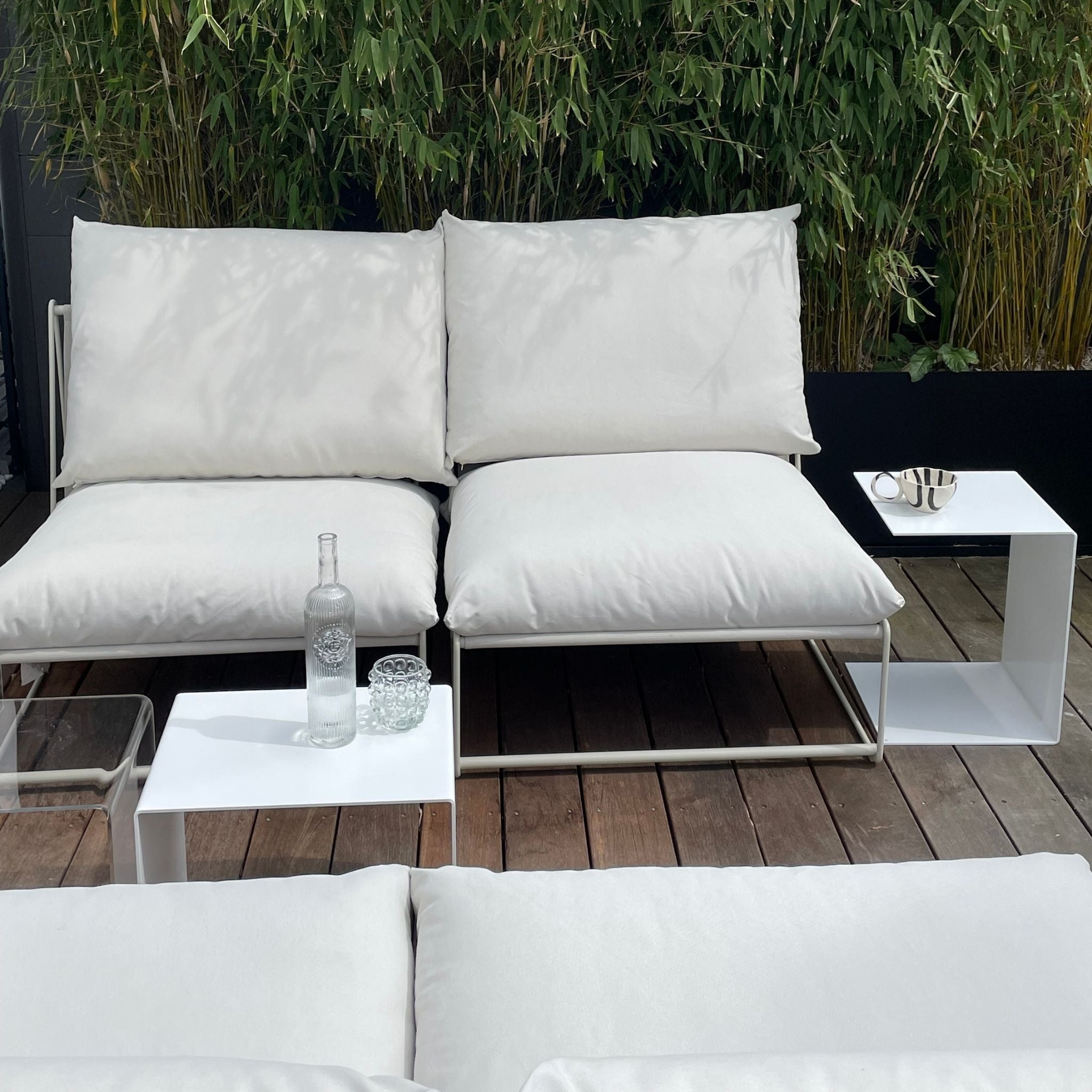 Weiße Beistelltische neben Outdoor-Lounge mit Kissen auf Holzterrasse, modernes Gartenmöbel-Design