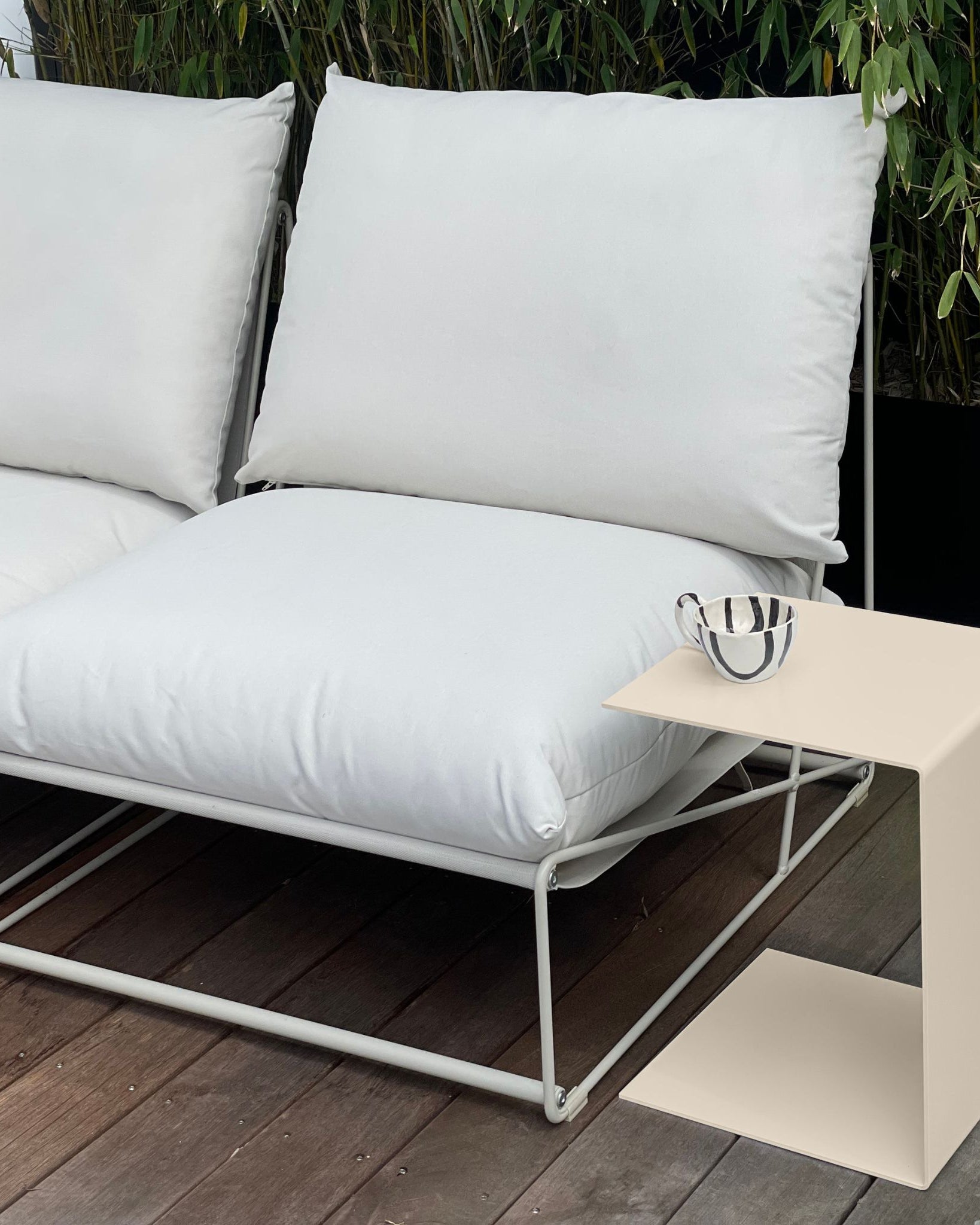 Cremeweißer Beistelltisch neben weißem Outdoor-Loungesofa auf Holzterrasse