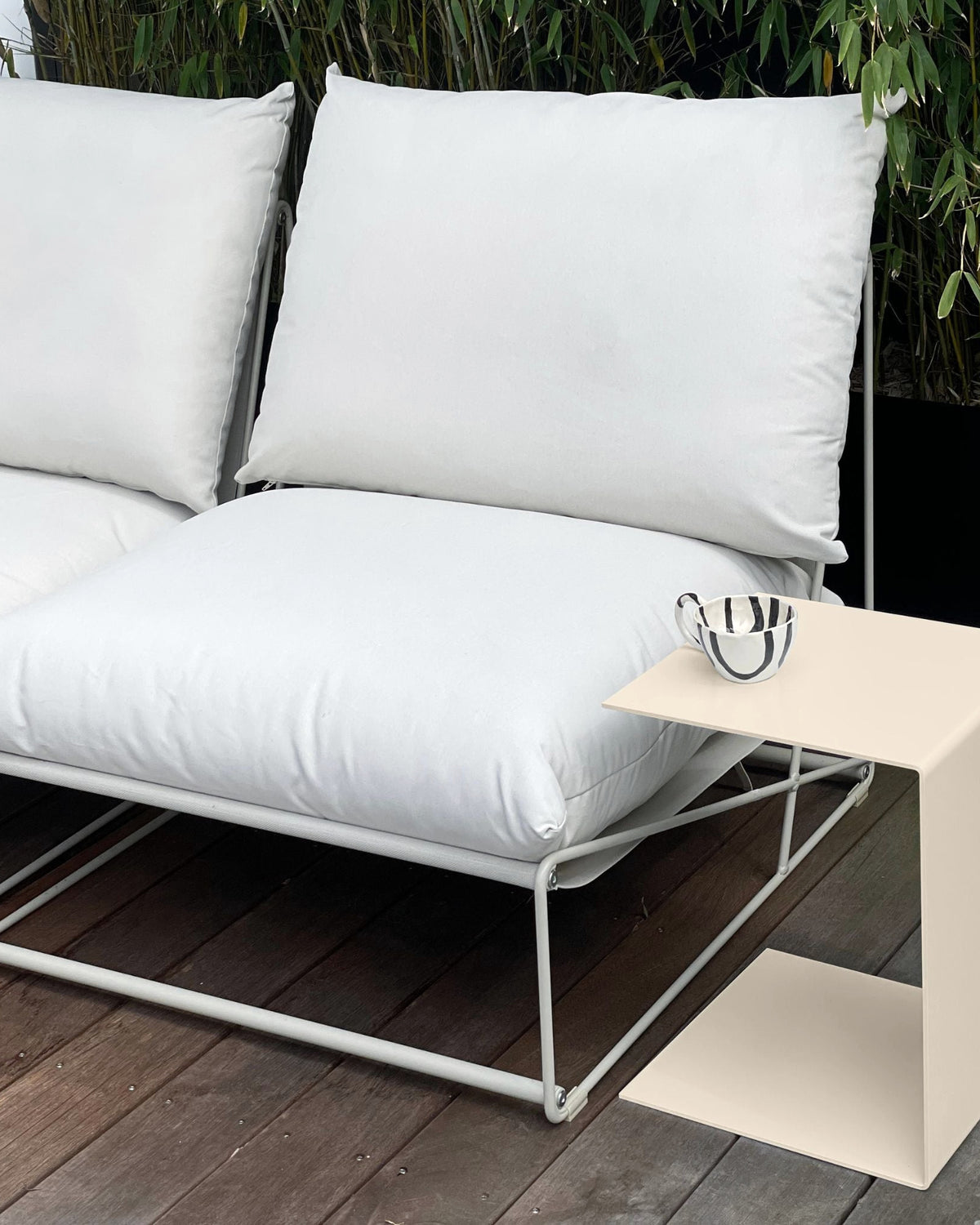 Cremeweißer Beistelltisch neben weißem Outdoor-Loungesofa auf Holzterrasse