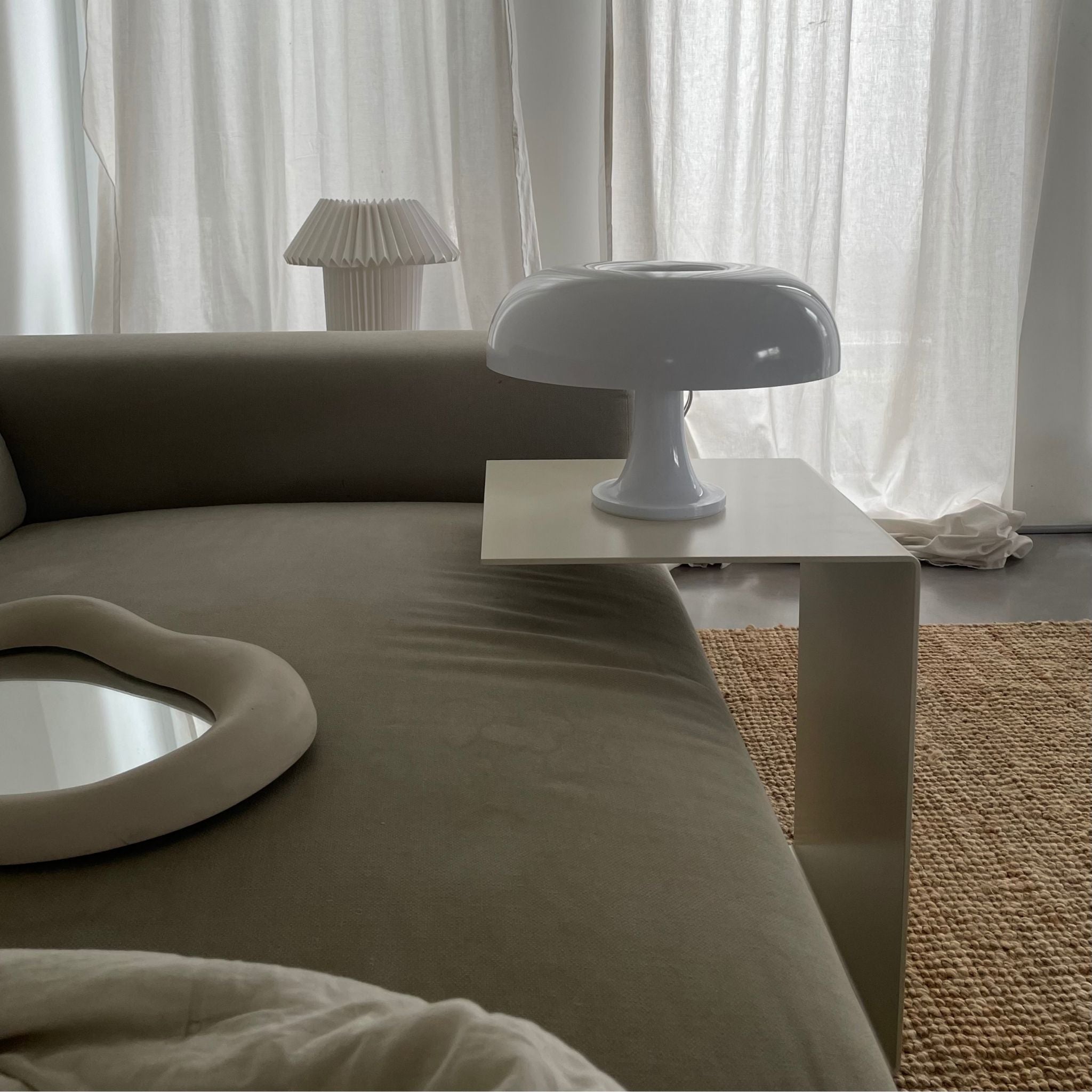 Cremeweißer Beistelltisch an Sofa mit Designerlampe und minimalistischem Wohnstil