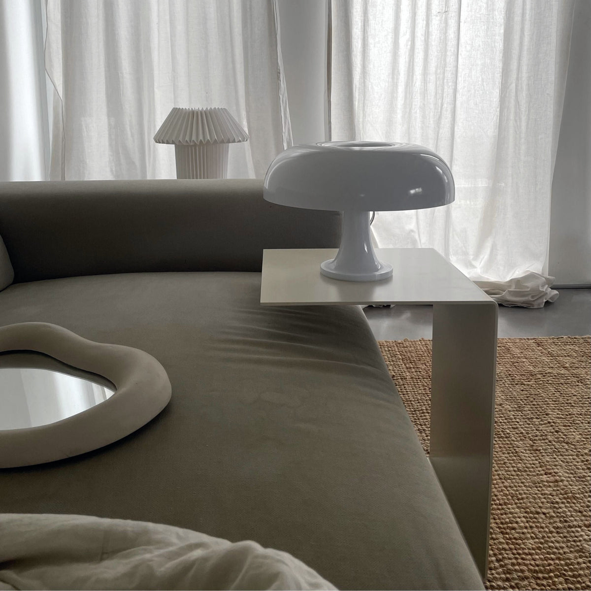 Cremeweißer Beistelltisch an Sofa mit Designerlampe und minimalistischem Wohnstil