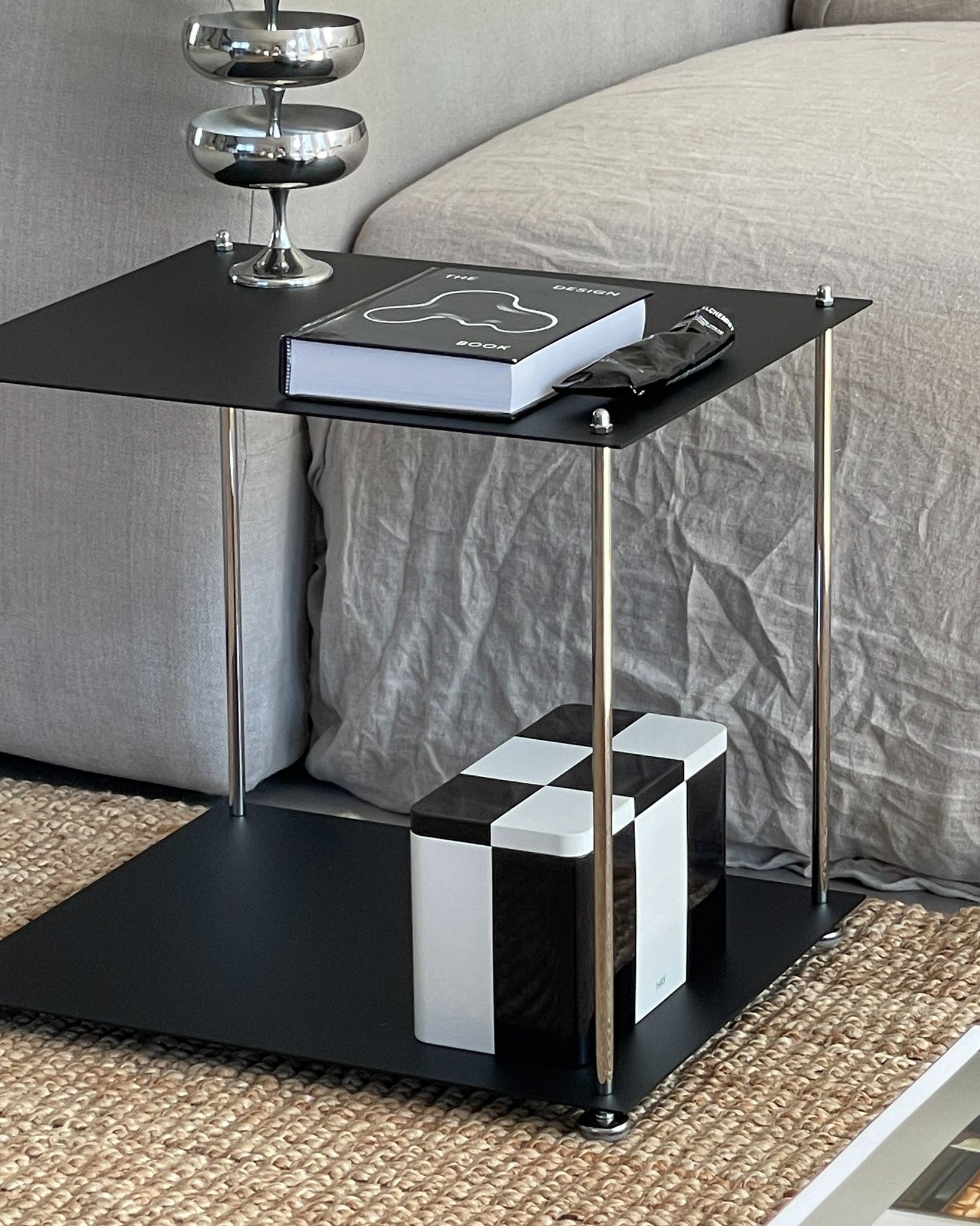 MODULUM Beistelltisch in Schwarz matt mit Pulverbeschichtung vor Sofa, dekoriert mit Buch und Designobjekten