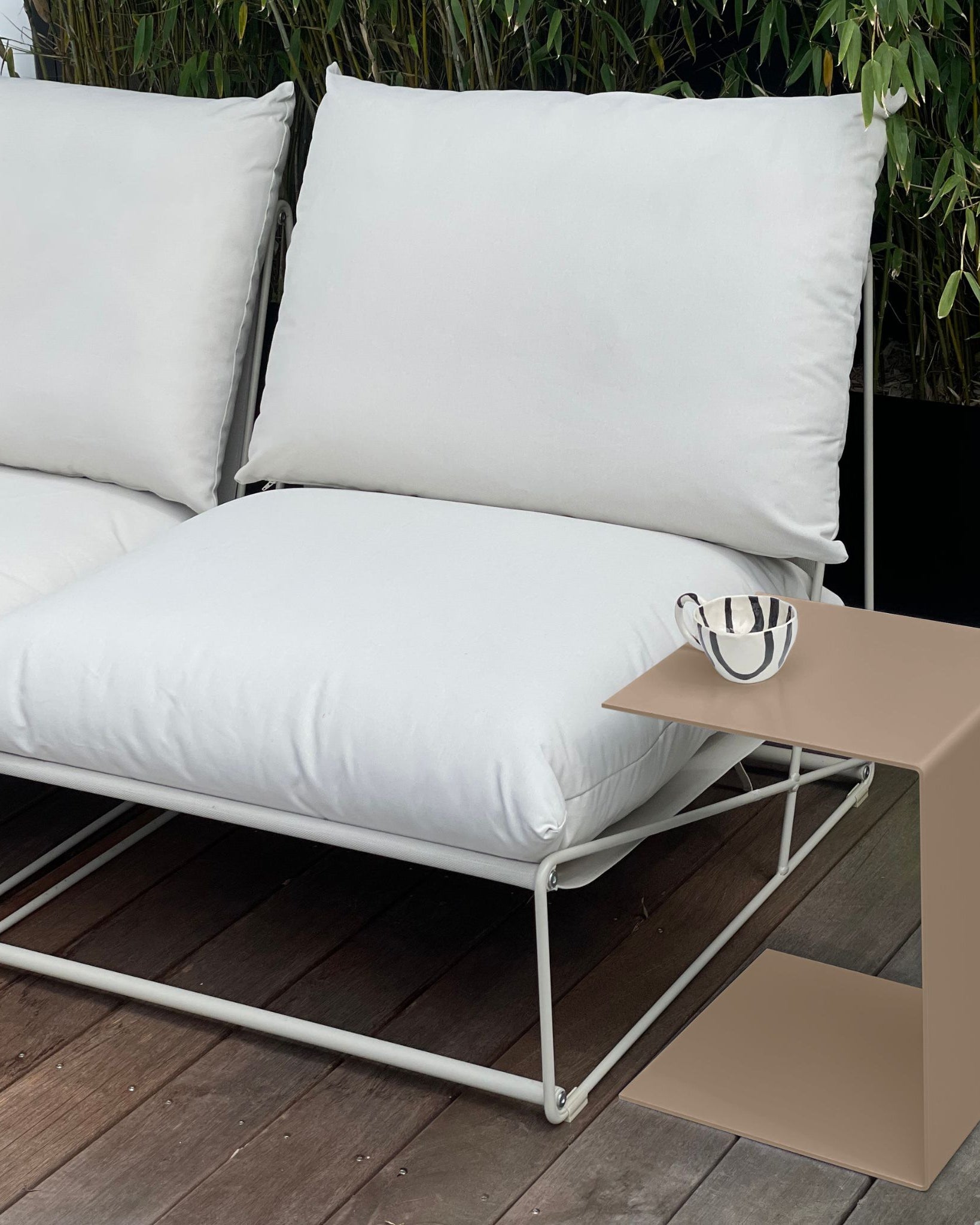 Moderner Beistelltisch in Graubeige neben weißem Outdoor-Sofa auf einer Holzterrasse