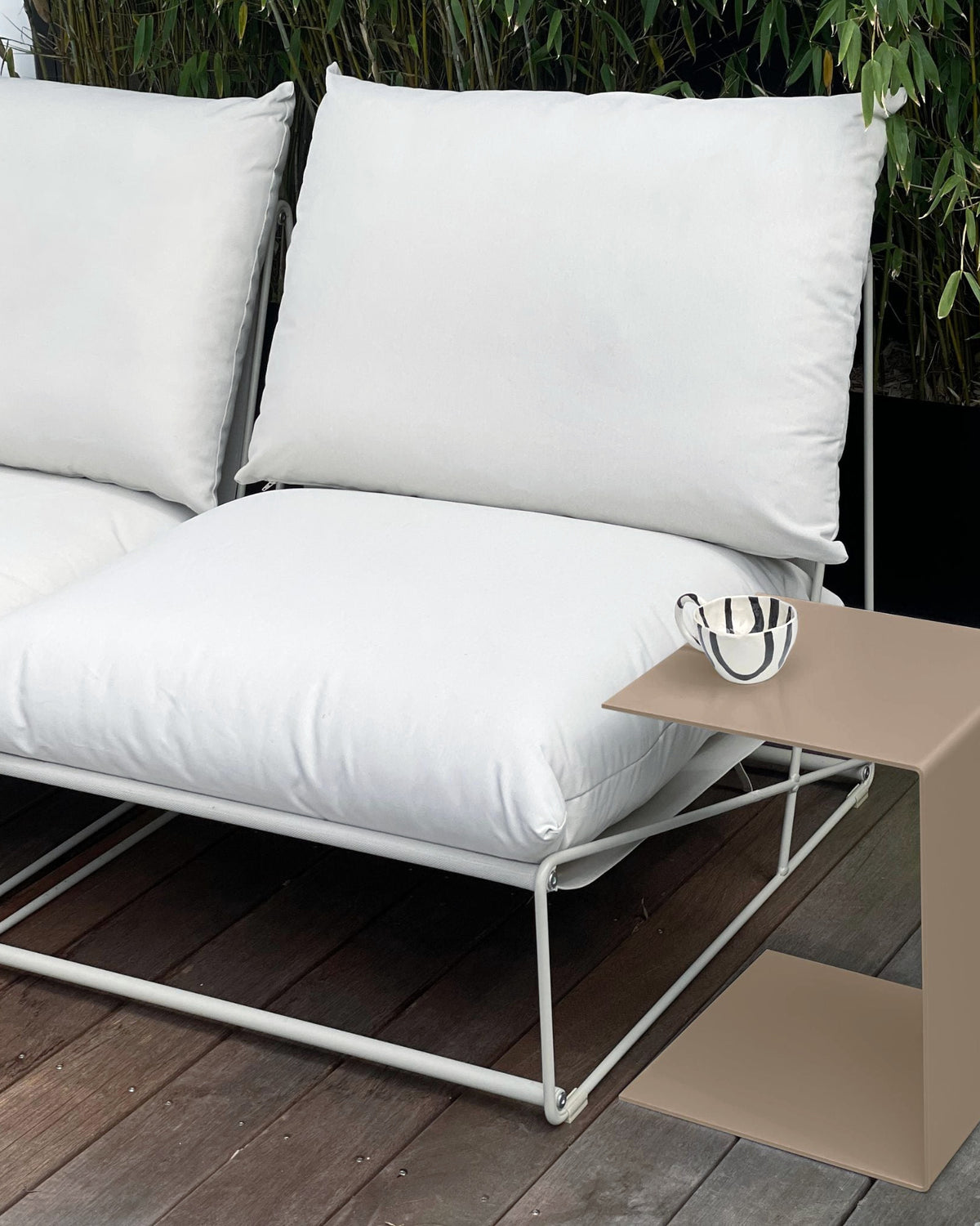 Moderner Beistelltisch in Graubeige neben weißem Outdoor-Sofa auf einer Holzterrasse