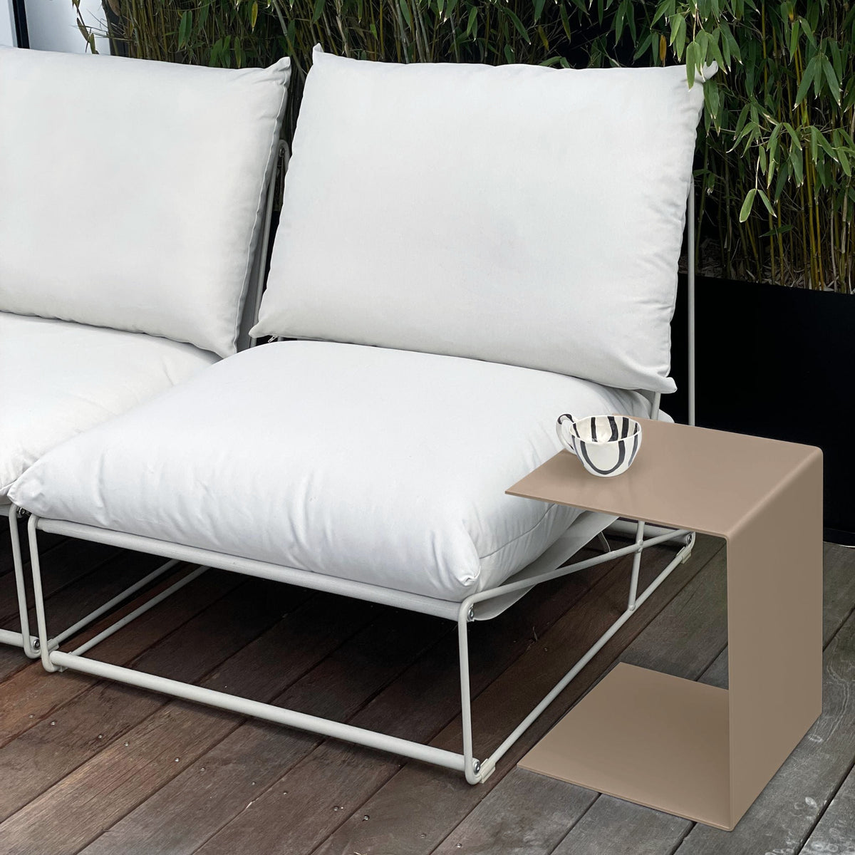 Moderner Beistelltisch in Graubeige neben weißem Outdoor-Sofa auf einer Holzterrasse