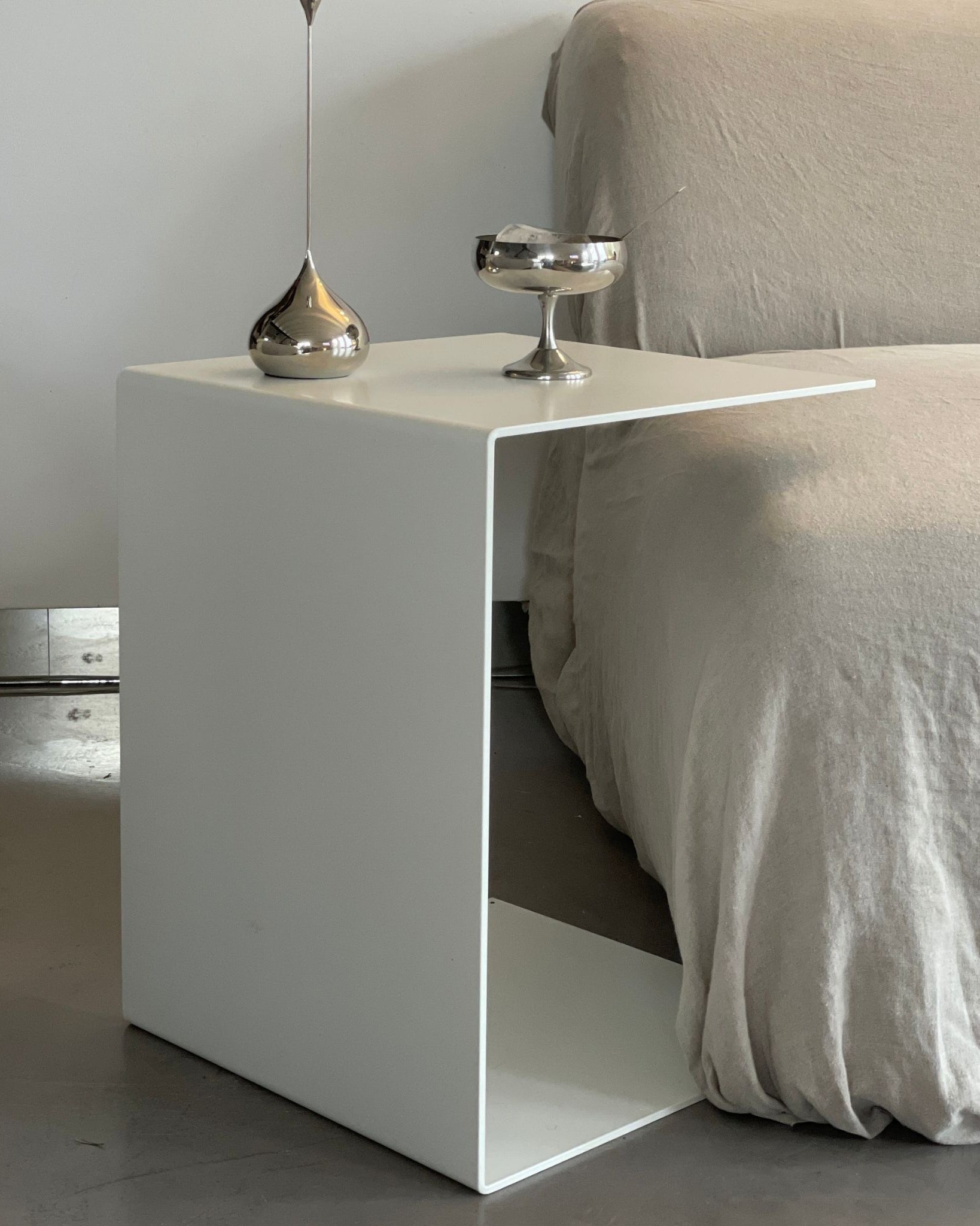 Minimalistischer weißer Beistelltisch neben einem Sofa mit Edelstahl-Deko