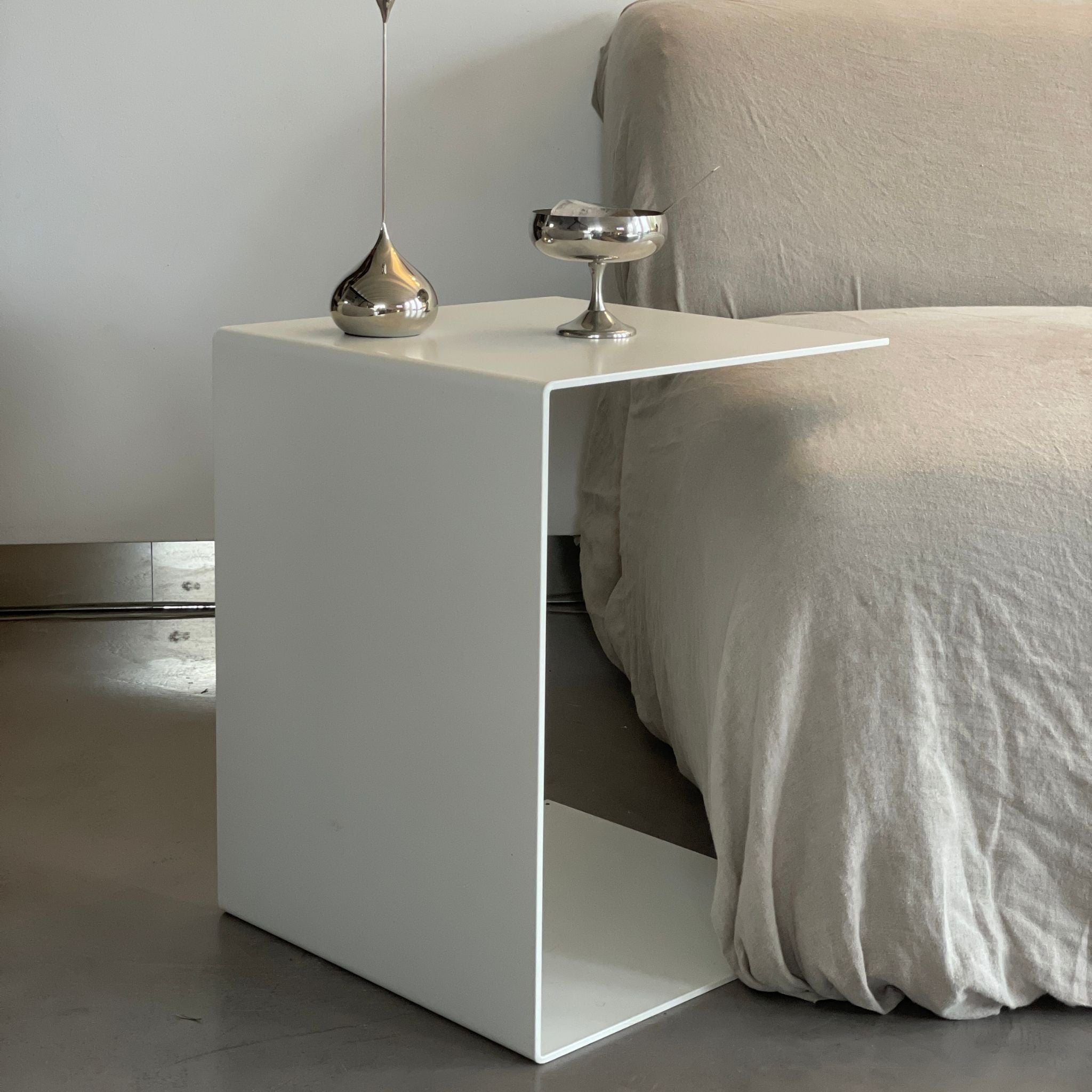 Minimalistischer weißer Beistelltisch neben einem Sofa mit Edelstahl-Deko