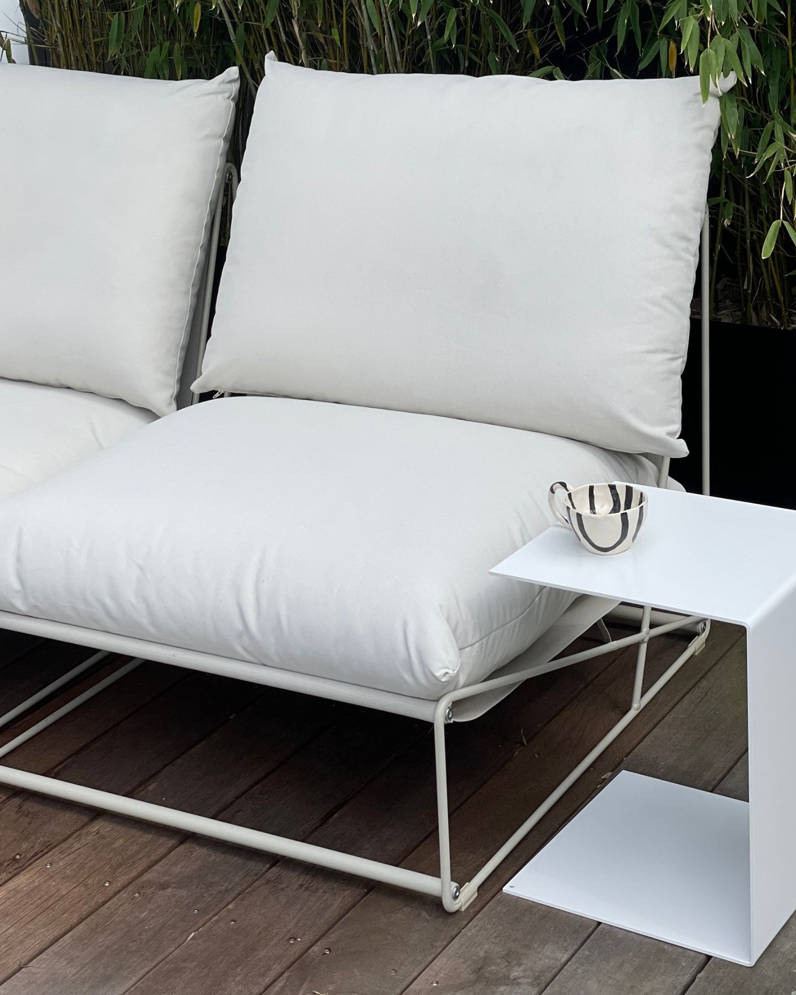 Weißer Beistelltisch neben Outdoor-Lounge mit Kissen auf Holzterrasse, modernes Gartenmöbel-Design