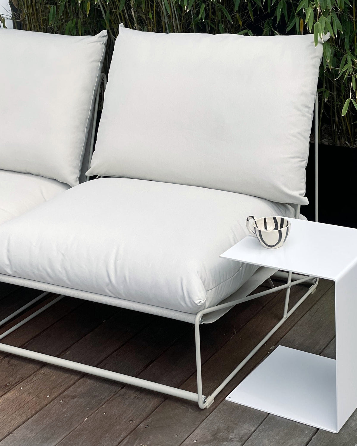 Weißer Beistelltisch neben Outdoor-Lounge mit Kissen auf Holzterrasse, modernes Gartenmöbel-Design