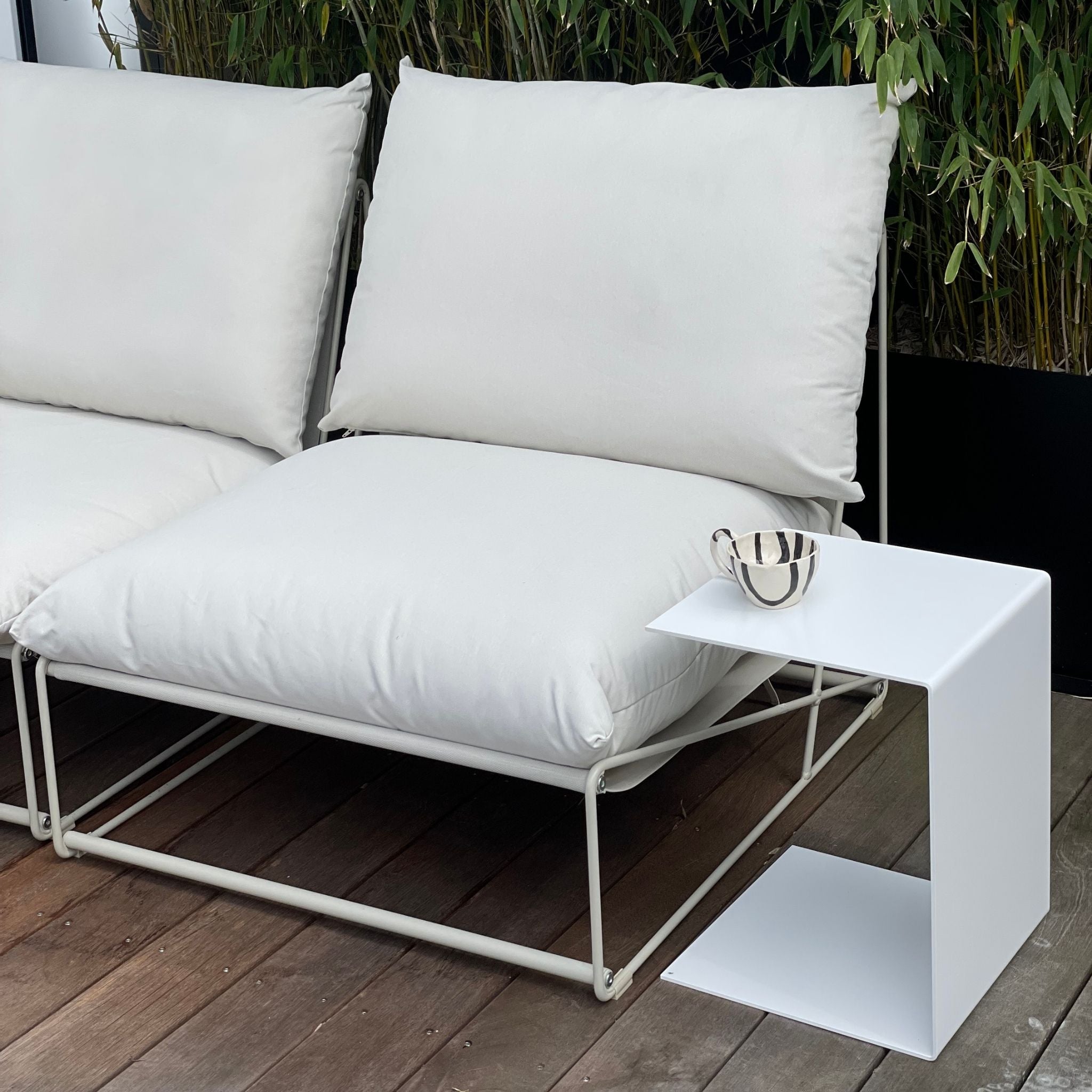 Weißer Beistelltisch neben Outdoor-Lounge mit Kissen auf Holzterrasse, modernes Gartenmöbel-Design