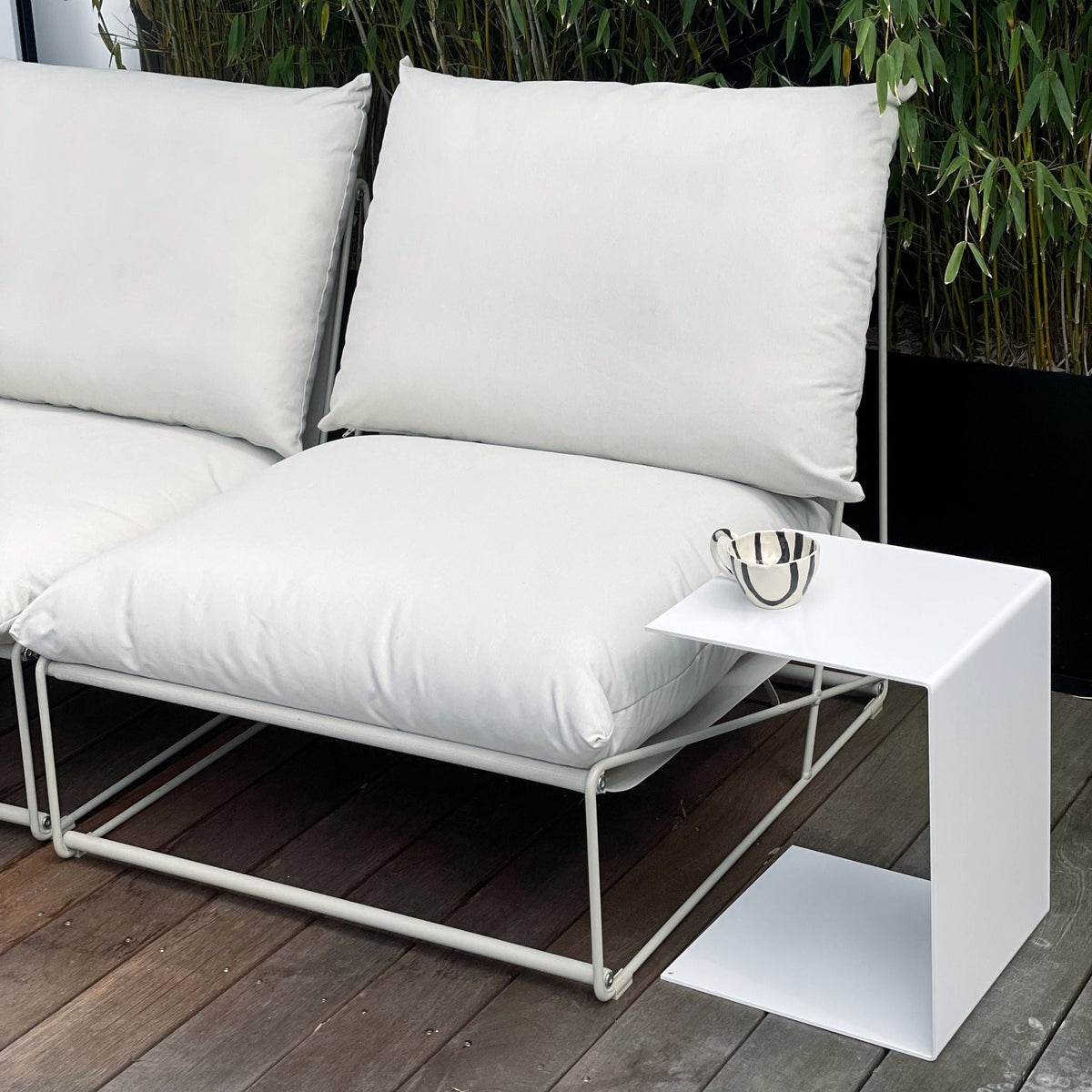 Weißer Beistelltisch neben Outdoor-Lounge mit Kissen auf Holzterrasse, modernes Gartenmöbel-Design