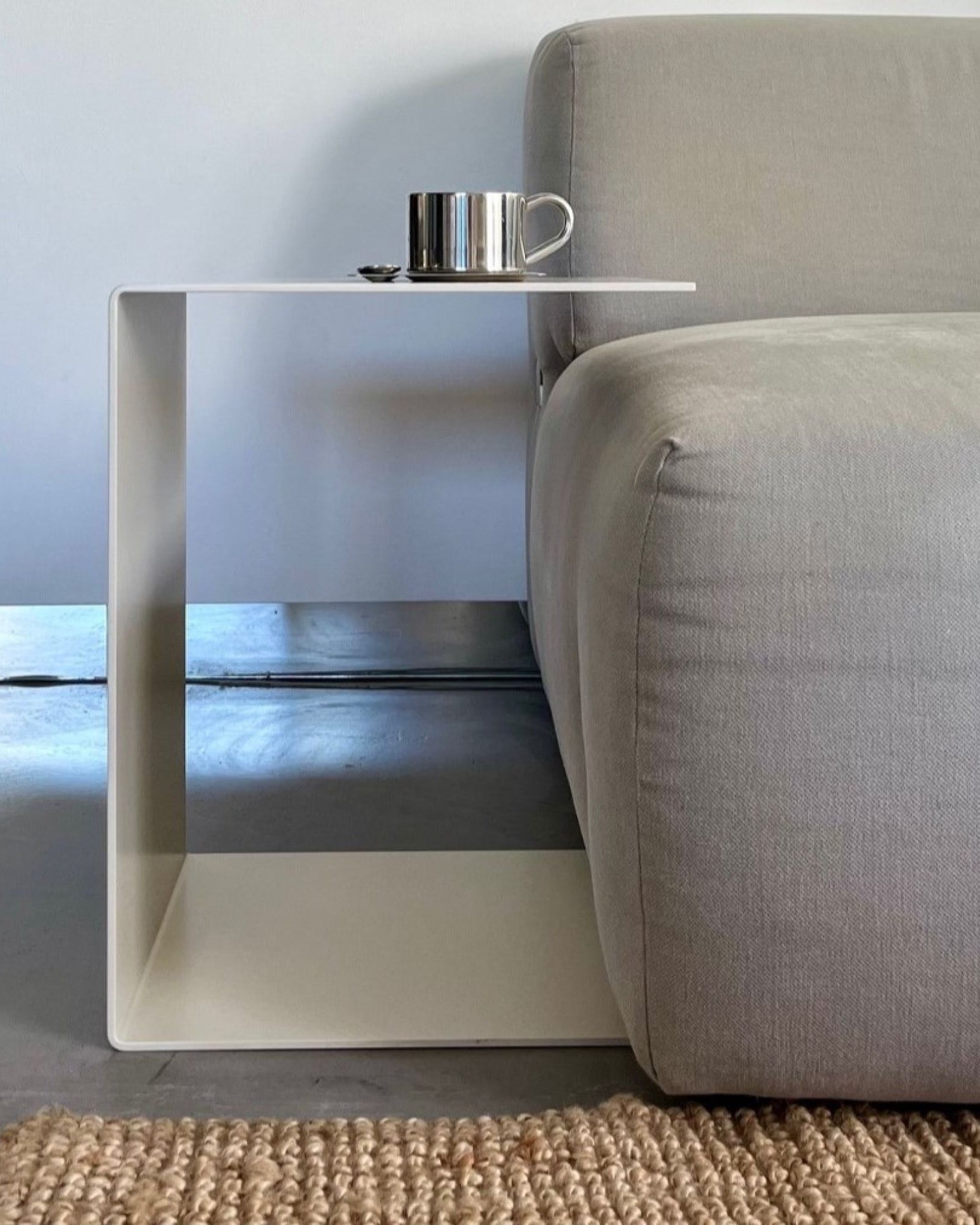 Cremeweißer BIG C Beistelltisch aus Stahl am grauen Sofa mit Tasse und Löffel, eingesetzt als Sofatisch auf hellem Teppich