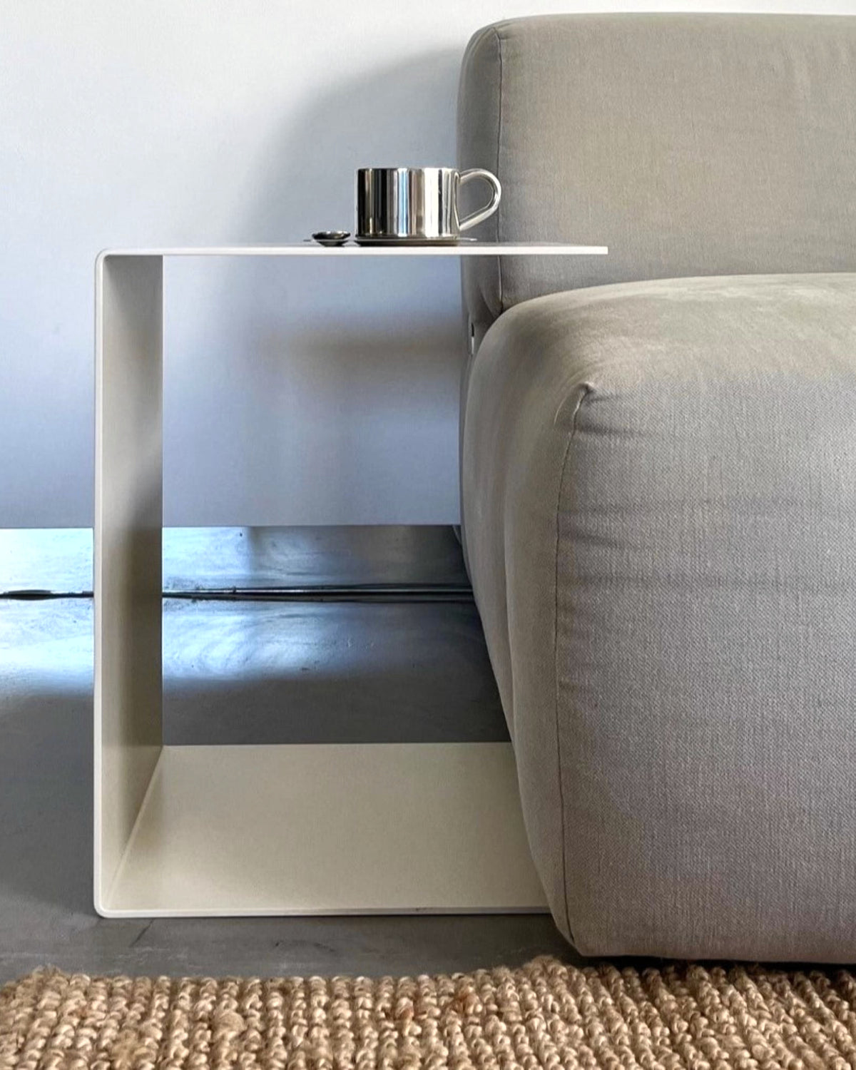 Cremeweißer BIG C Beistelltisch aus Stahl am grauen Sofa mit Tasse und Löffel, eingesetzt als Sofatisch auf hellem Teppich
