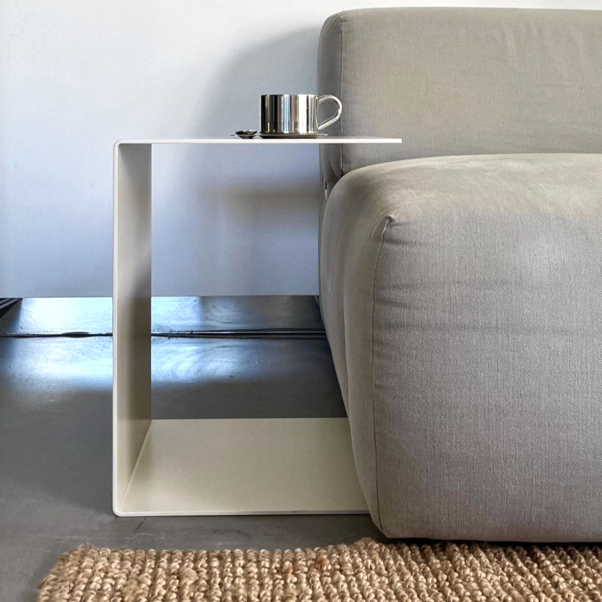 Cremeweißer BIG C Beistelltisch aus Stahl am grauen Sofa mit Tasse und Löffel, eingesetzt als Sofatisch auf hellem Teppich