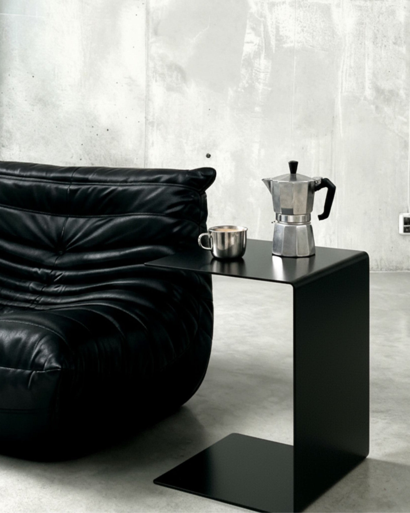 BIG C Beistelltisch in schwarz matt neben schwarzem Ledersofa mit Espressokanne und Tasse auf Betonboden