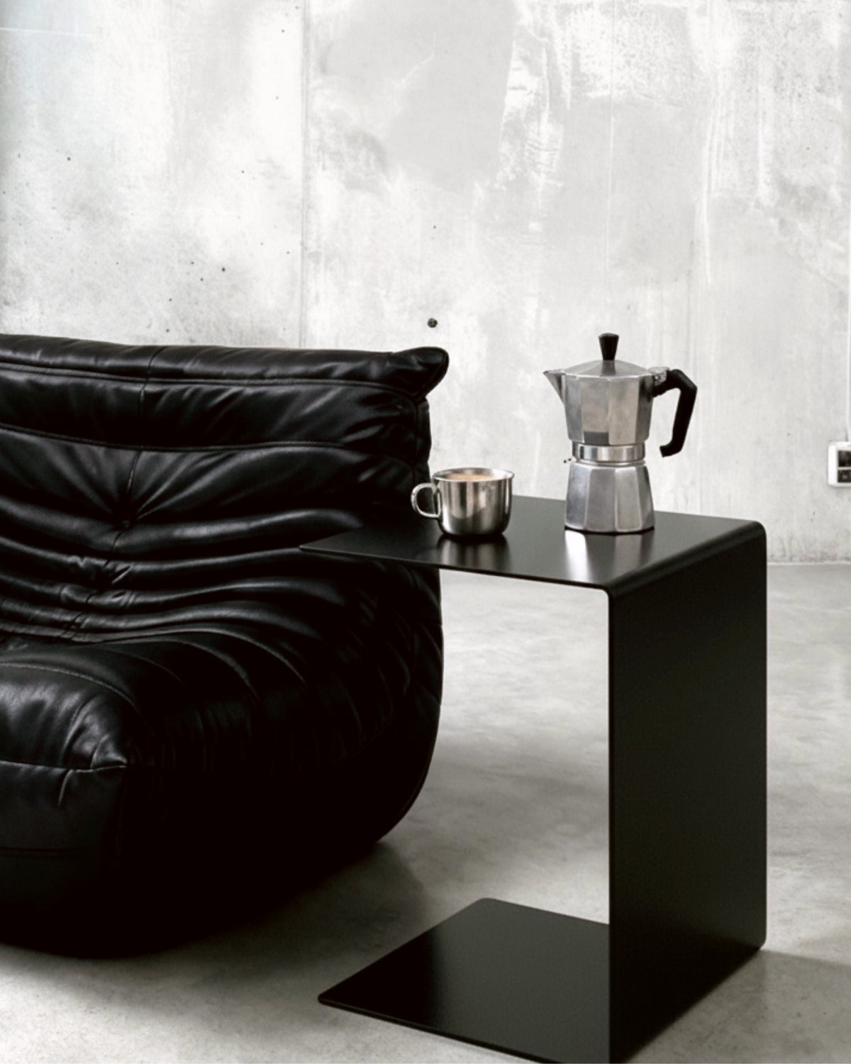 BIG C Beistelltisch in schwarz matt neben schwarzem Ledersofa mit Espressokanne und Tasse auf Betonboden