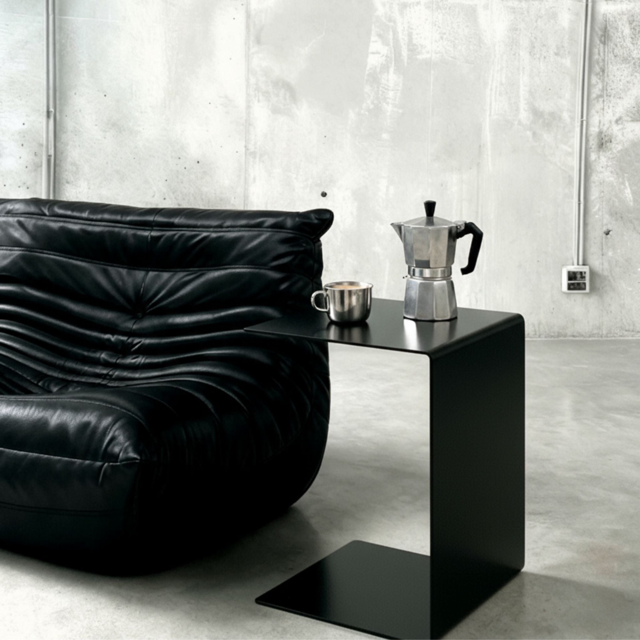 BIG C Beistelltisch in schwarz matt neben schwarzem Ledersofa mit Espressokanne und Tasse auf Betonboden