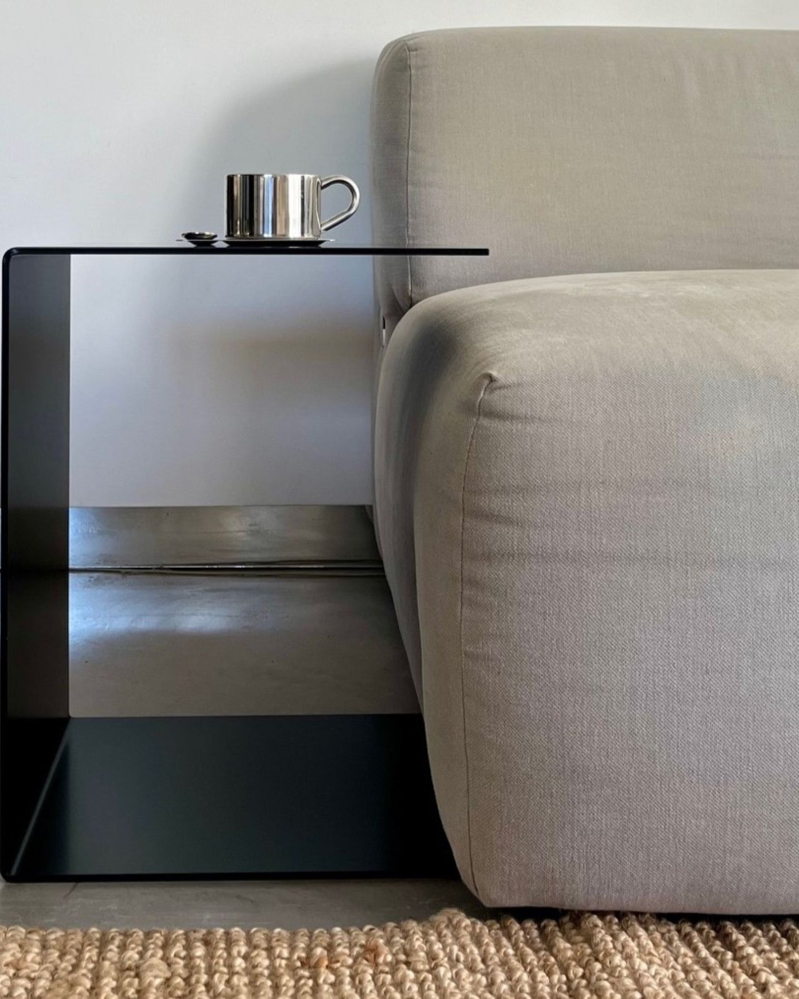 Schwarzer BIG C Beistelltisch aus Stahl als Sofatisch mit Tassenablage, bündig an graues Sofa gestellt auf Juteteppich