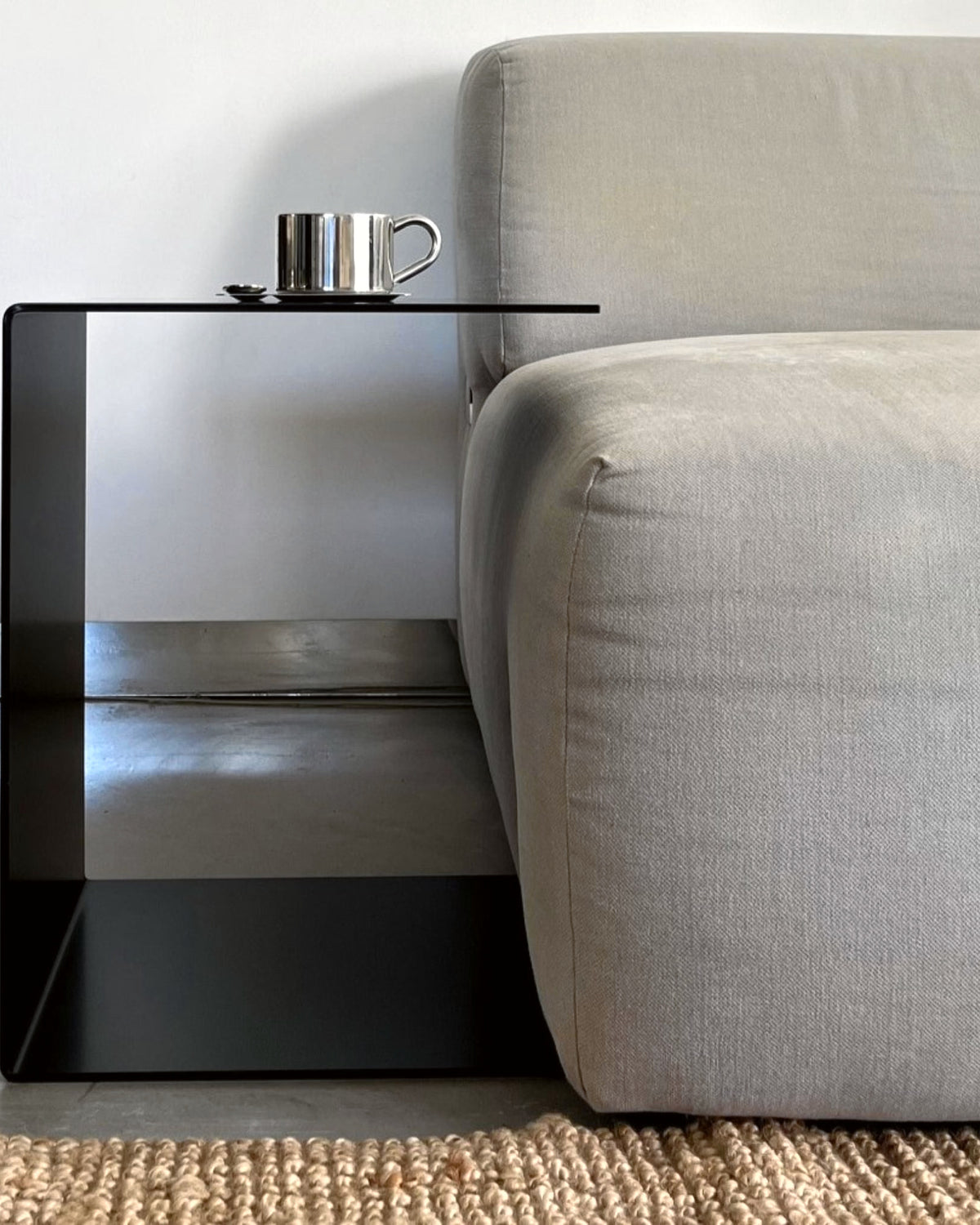 Schwarzer BIG C Beistelltisch aus Stahl als Sofatisch mit Tassenablage, bündig an graues Sofa gestellt auf Juteteppich