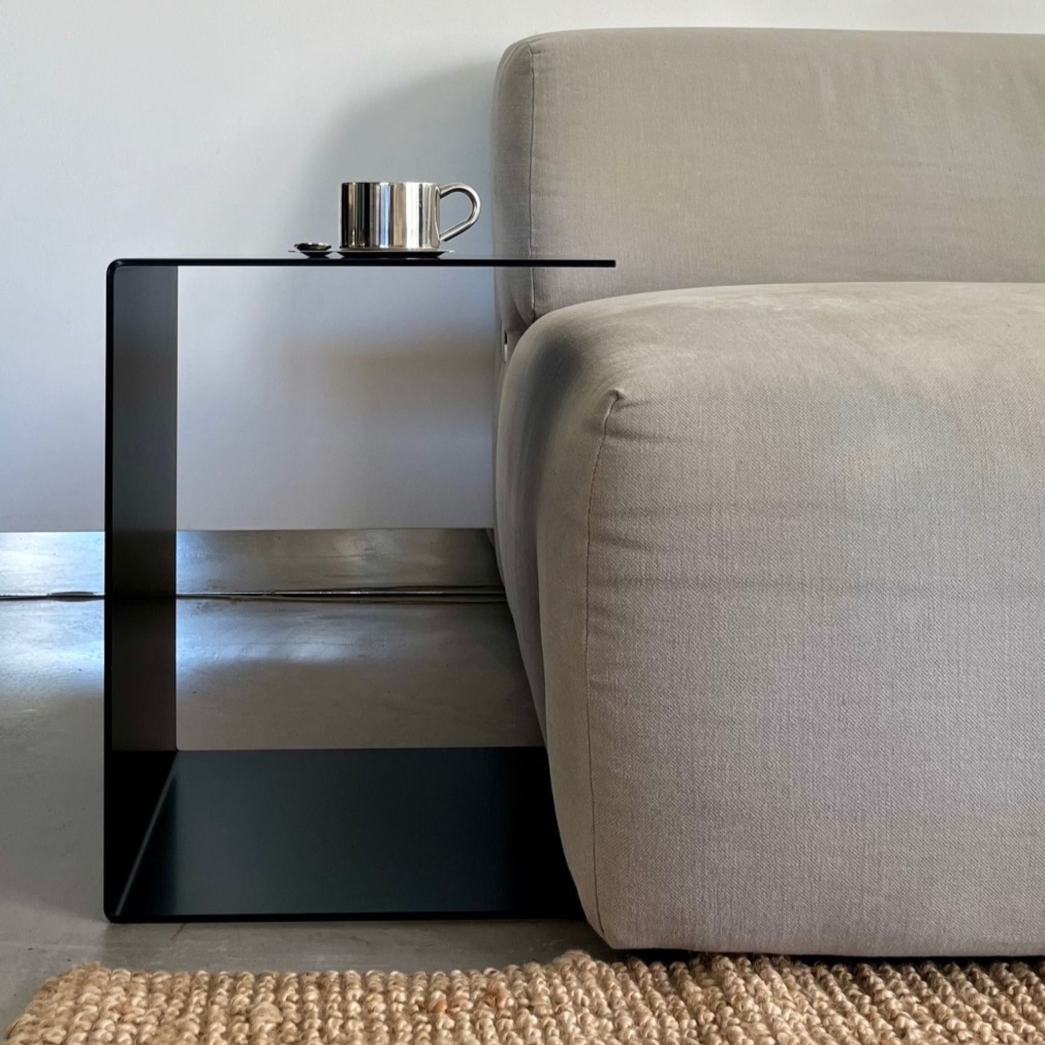 Schwarzer BIG C Beistelltisch aus Stahl als Sofatisch mit Tassenablage, bündig an graues Sofa gestellt auf Juteteppich