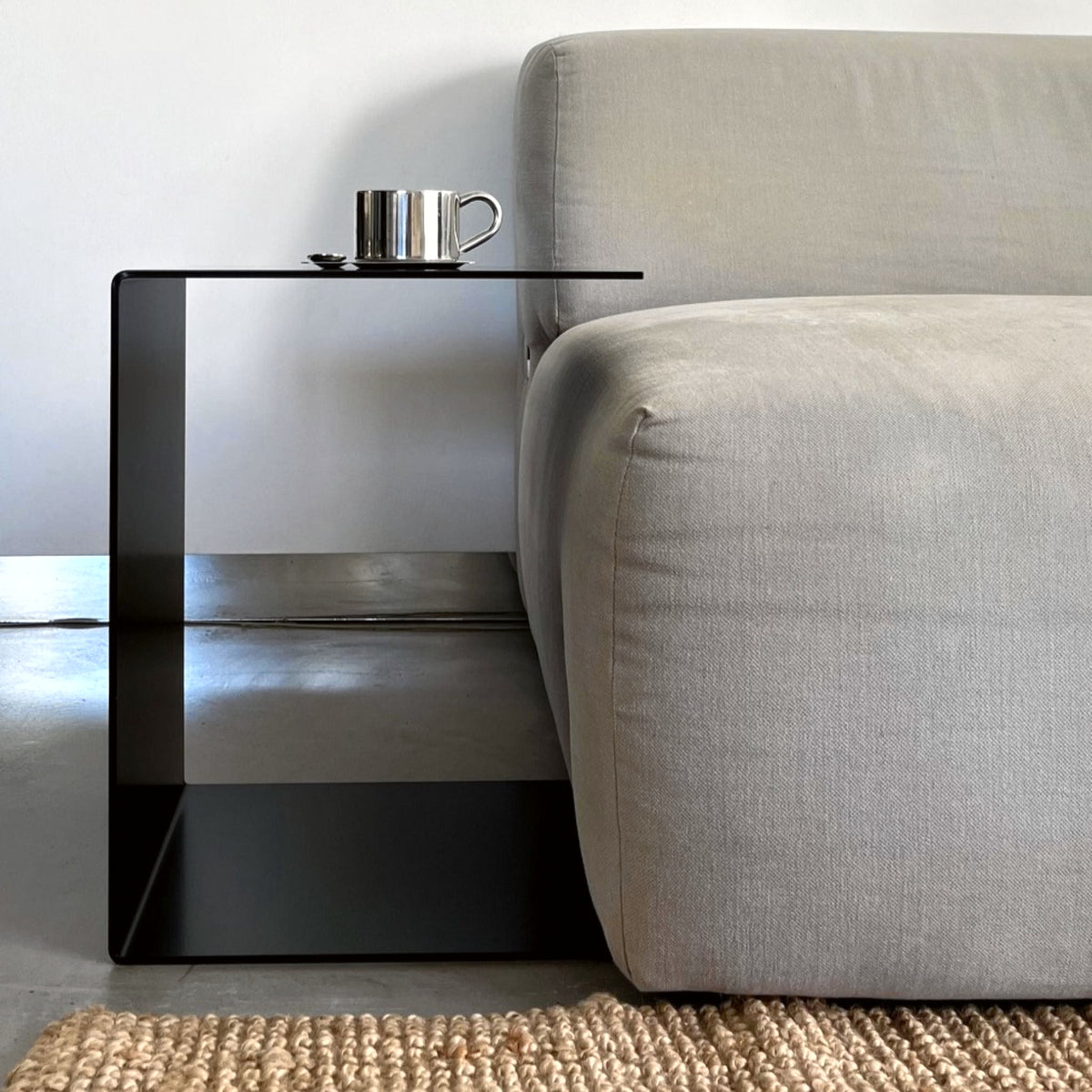 Schwarzer BIG C Beistelltisch aus Stahl als Sofatisch mit Tassenablage, bündig an graues Sofa gestellt auf Juteteppich