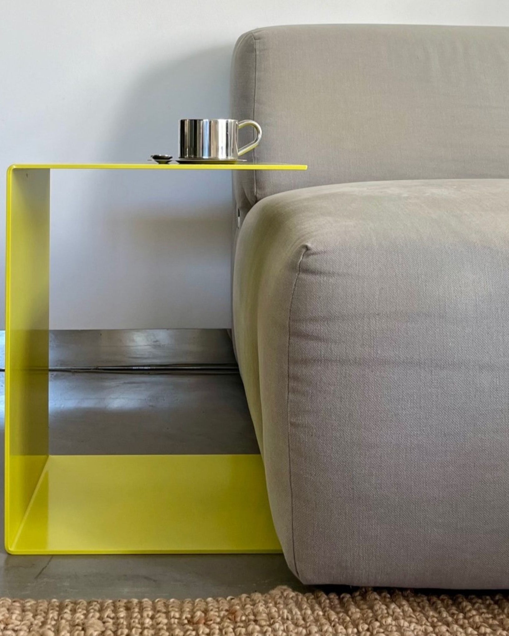 Schwefelgelber BIG C Beistelltisch aus Stahl am Sofa, als Sofatisch genutzt mit Edelstahltasse und Löffel auf Teppichboden