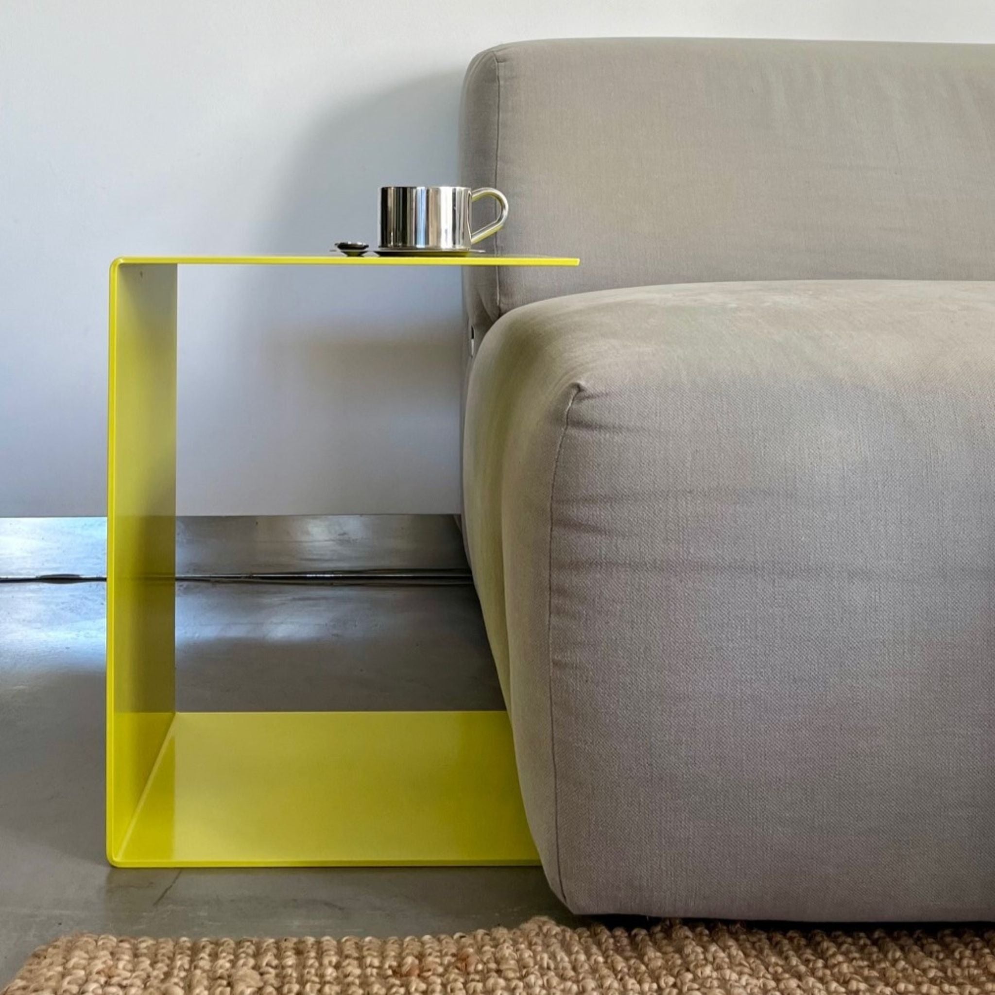 Schwefelgelber BIG C Beistelltisch aus Stahl am Sofa, als Sofatisch genutzt mit Edelstahltasse und Löffel auf Teppichboden