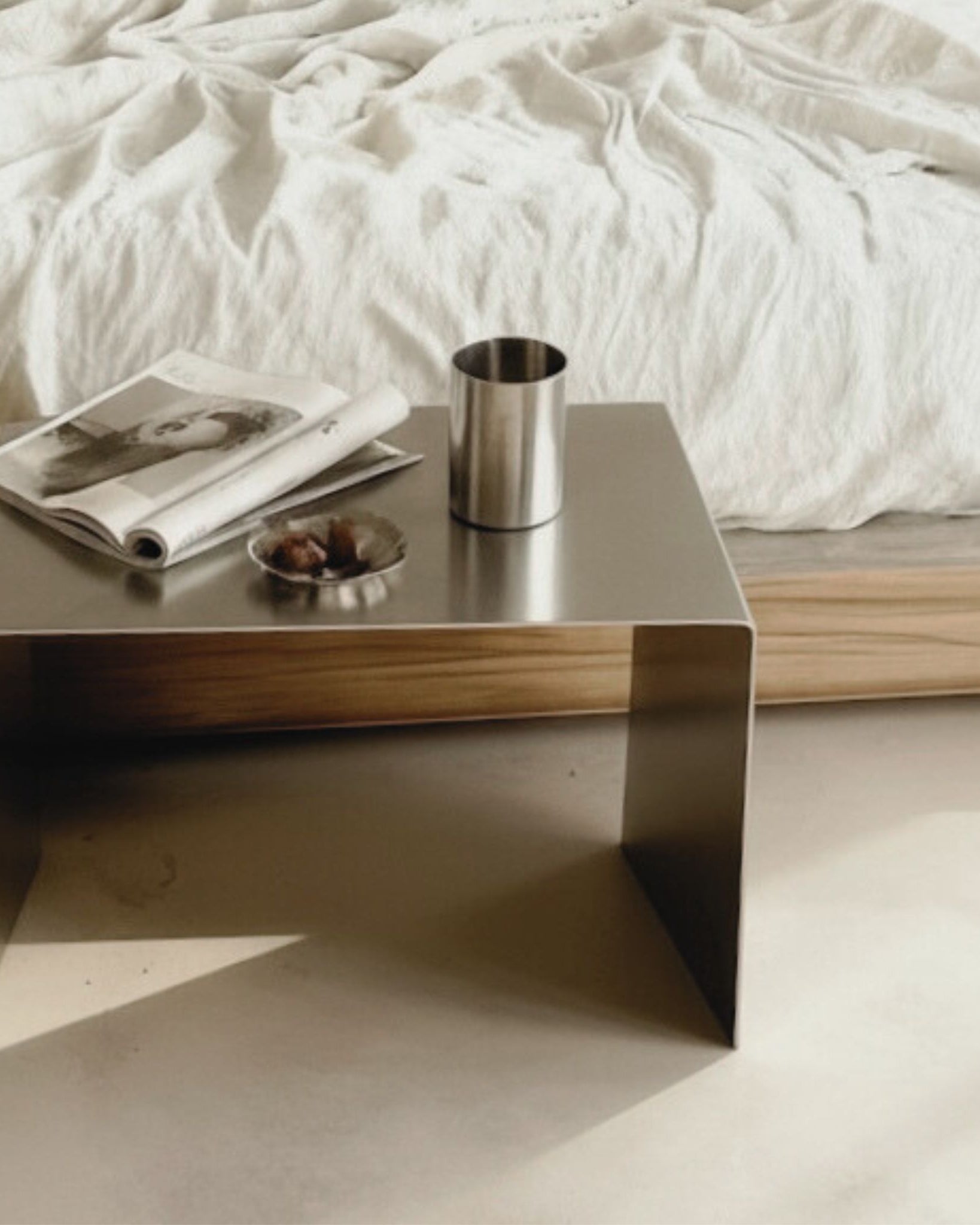 Brushed C Beistelltisch aus gebürstetem Edelstahl als minimalistischer Nachttisch mit Magazin und Becher im Schlafzimmer