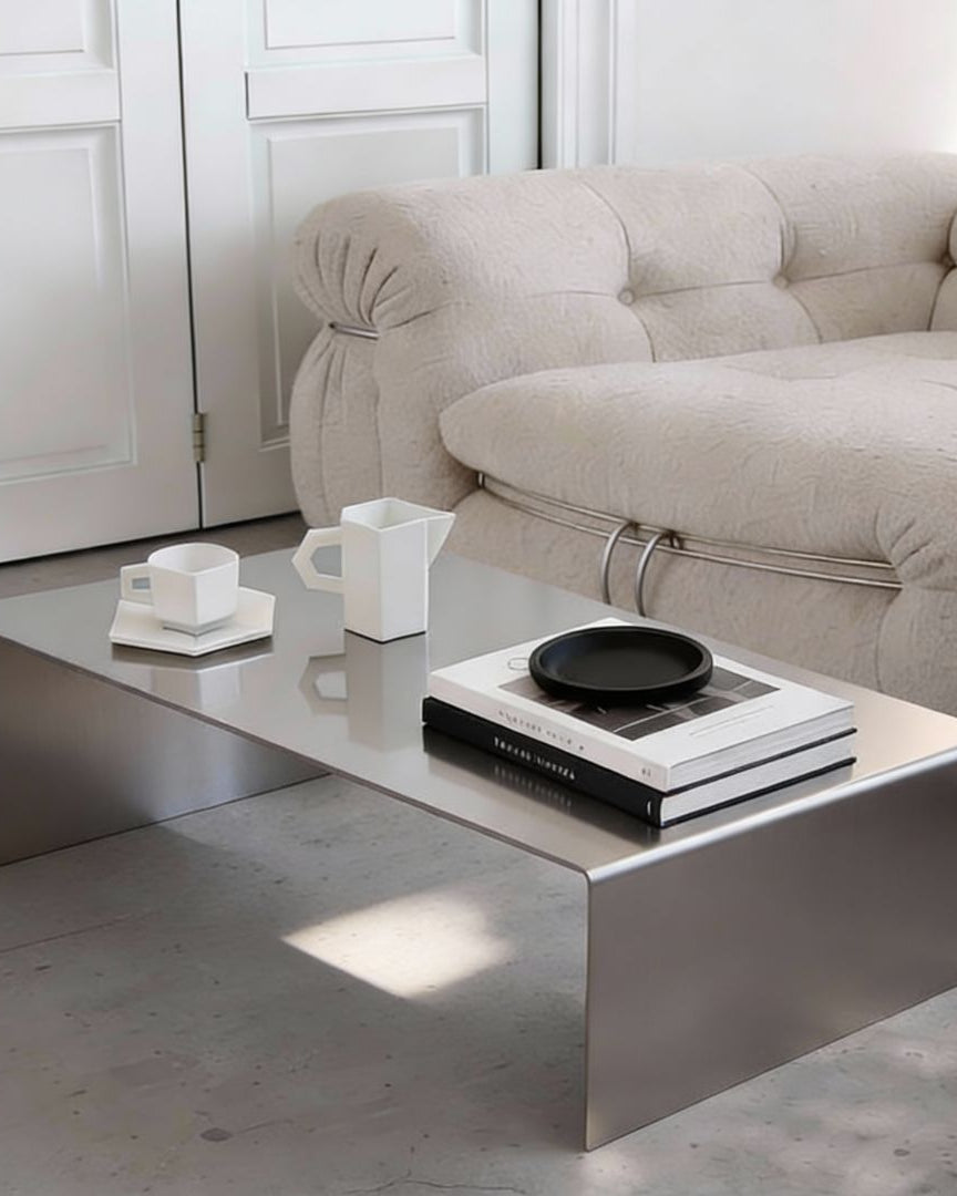 Brushed C Long Couchtisch aus gebürstetem Edelstahl mit Büchern und Keramik im minimalistischen Wohnzimmer vor Sofa