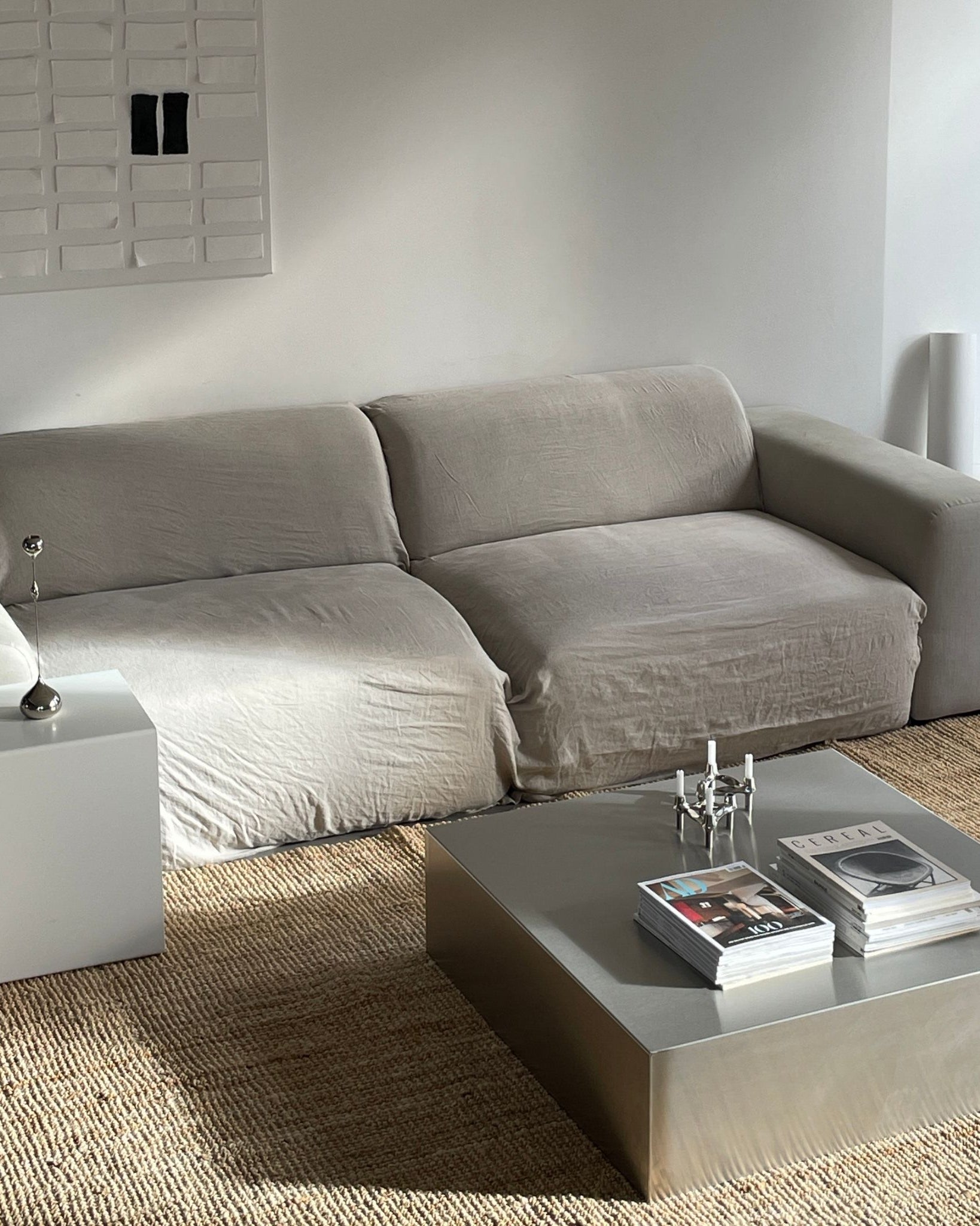 Gebürsteter Edelstahl-Couchtisch mit Magazinen und Kerzenhalter vor grauer Couch auf Naturteppich