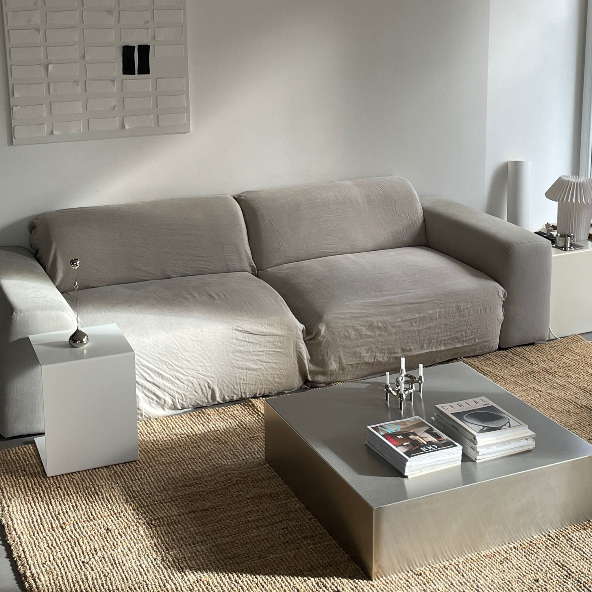 Gebürsteter Edelstahl-Couchtisch mit Magazinen und Kerzenhalter vor grauer Couch auf Naturteppich