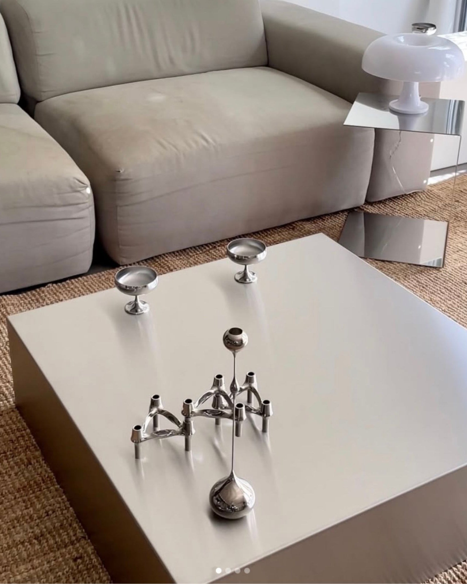 Moderner Couchtisch aus gebürstetem Edelstahl mit Design-Kerzenhaltern vor grauer Couch auf Naturteppich