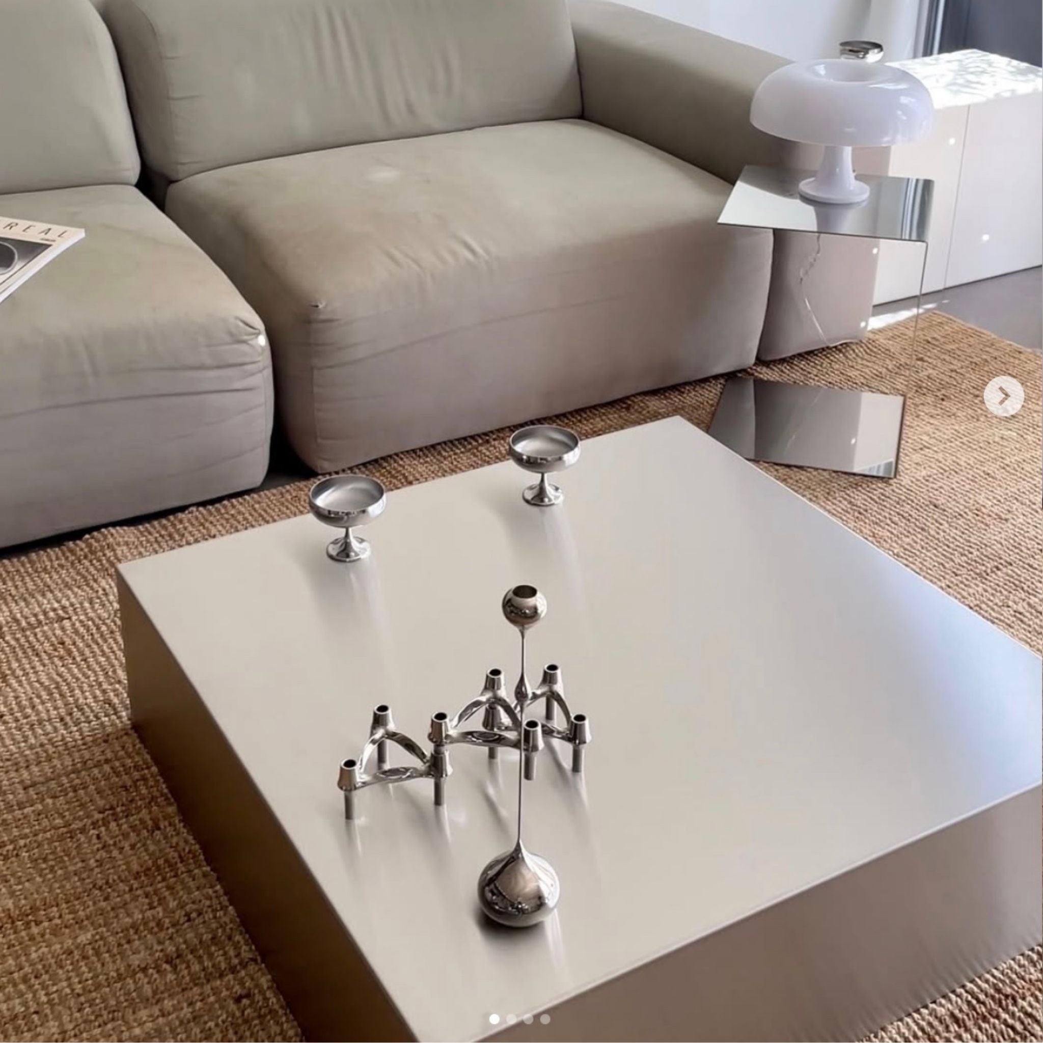 Moderner Couchtisch aus gebürstetem Edelstahl mit Design-Kerzenhaltern vor grauer Couch auf Naturteppich