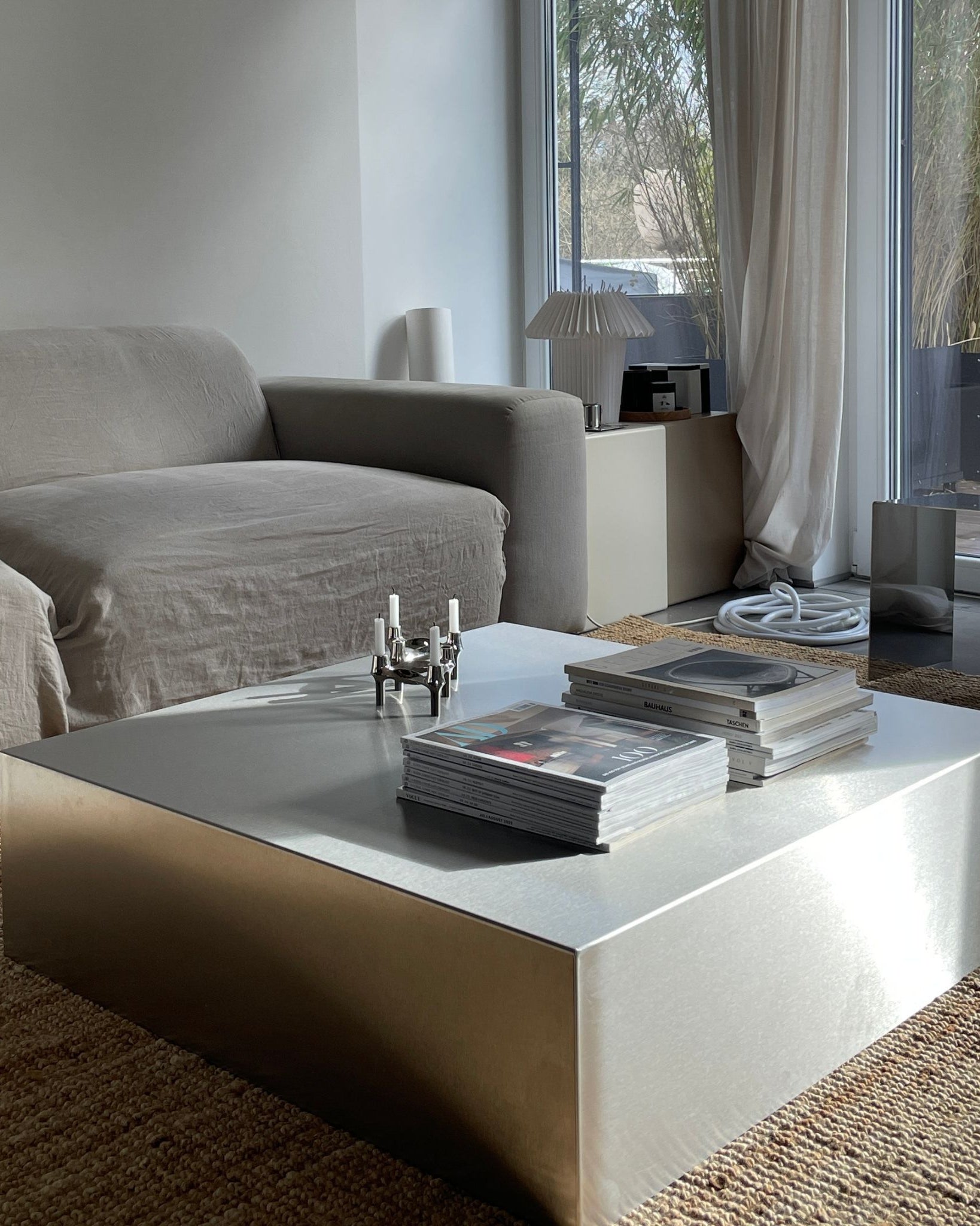 Couchtisch aus gebürstetem Edelstahl mit Magazinen und Kerzenhalter in modernem Wohnzimmer mit grauer Couch