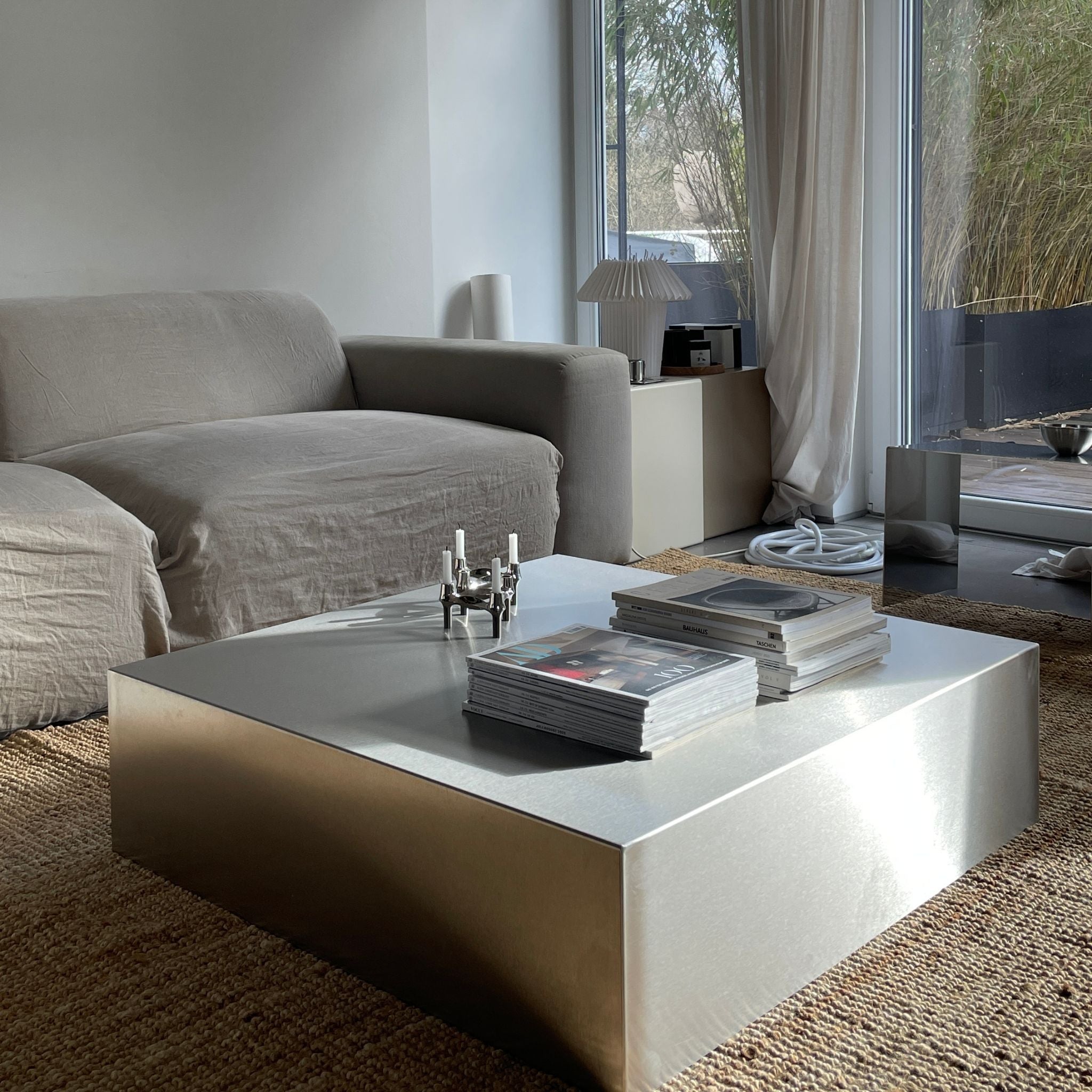 Couchtisch aus gebürstetem Edelstahl mit Magazinen und Kerzenhalter in modernem Wohnzimmer mit grauer Couch