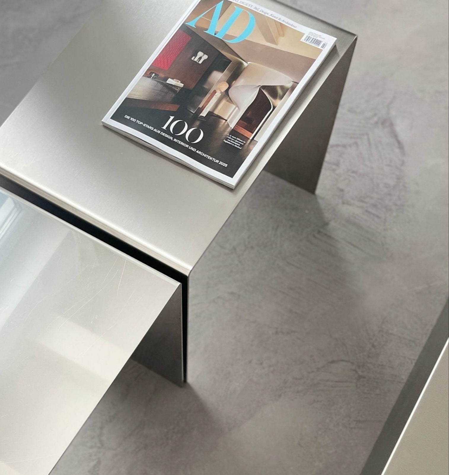 Moderner Couchtisch aus Edelstahl mit gebürsteter und spiegelpolierter Oberfläche auf Betonboden