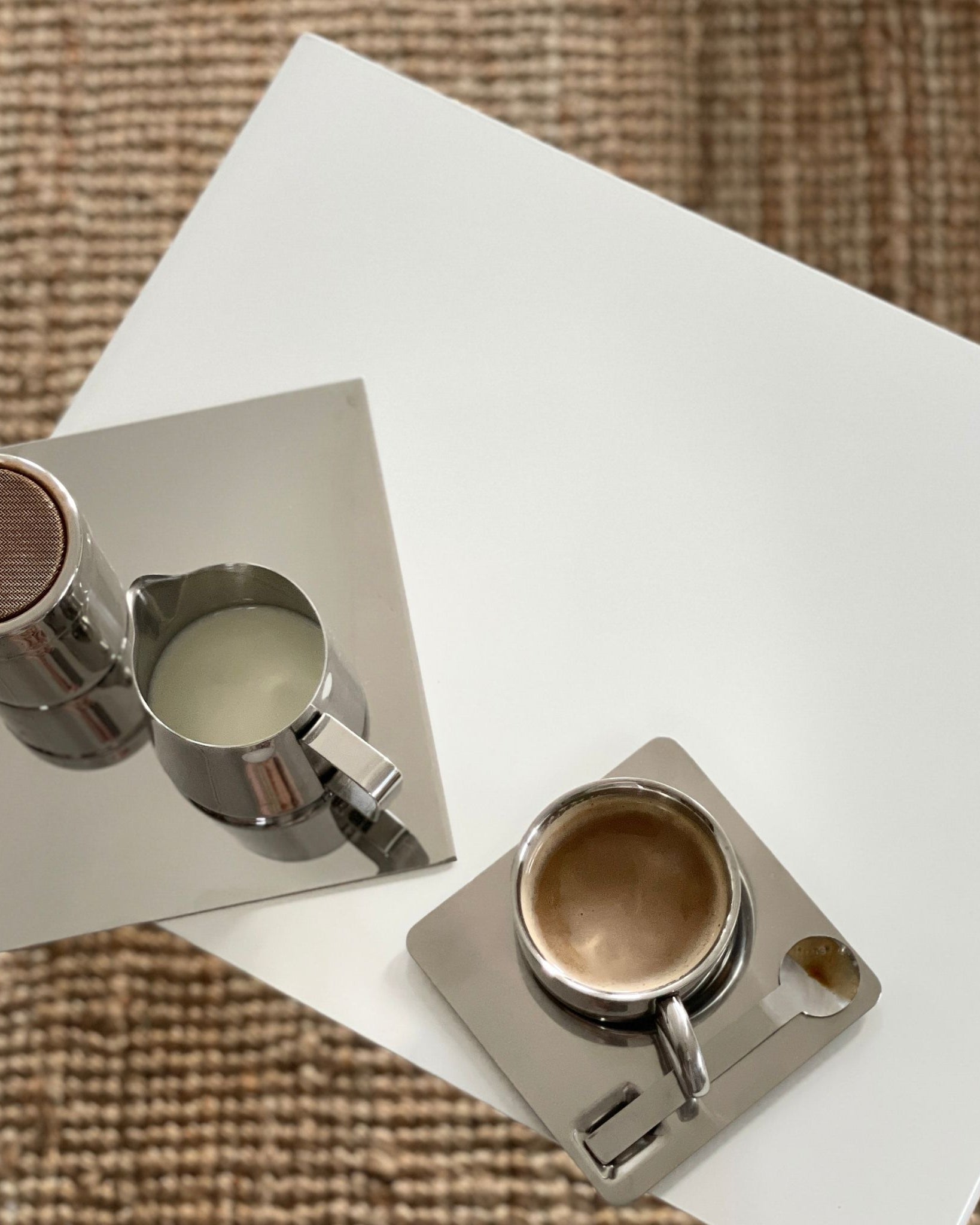 Detailaufnahme eines weißen Couchtisches mit Espressotasse, Milchkännchen und Spiegelplatte auf Naturteppich