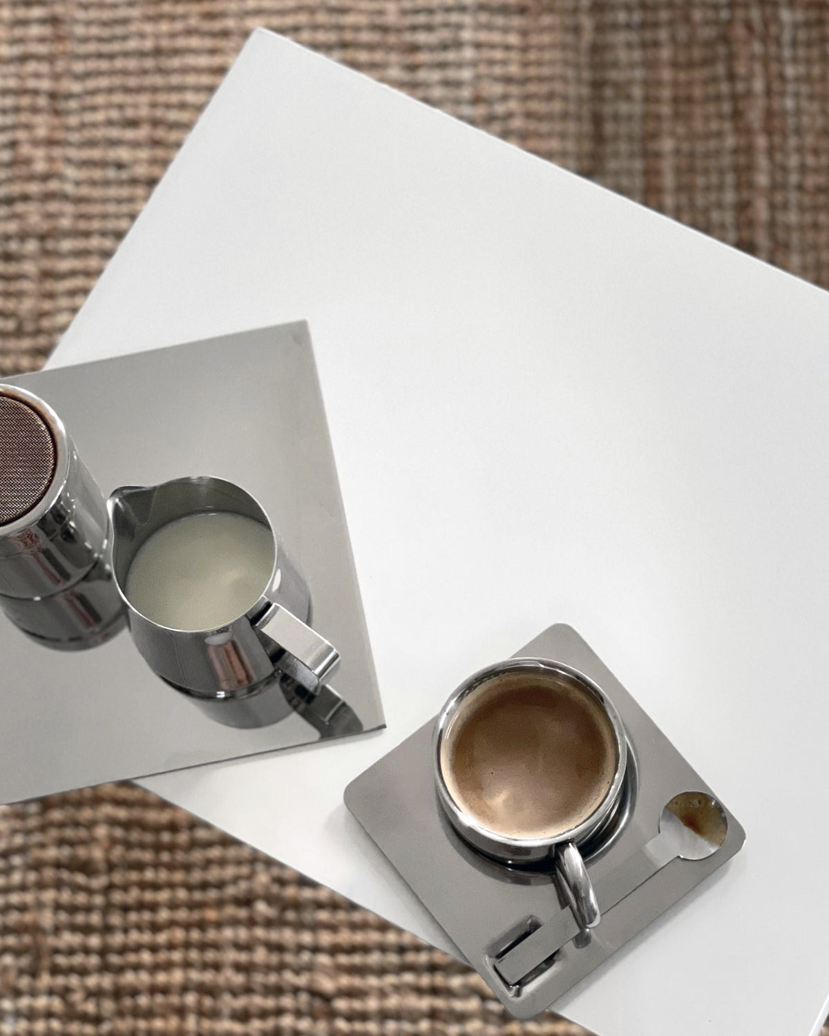 Detailaufnahme eines weißen Couchtisches mit Espressotasse, Milchkännchen und Spiegelplatte auf Naturteppich